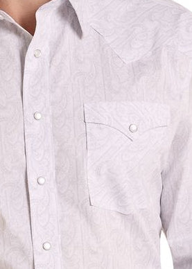 A man wearing a light-colored, long-sleeve western-style button-down shirt with two chest pockets, paired with blue jeans and a dark belt.