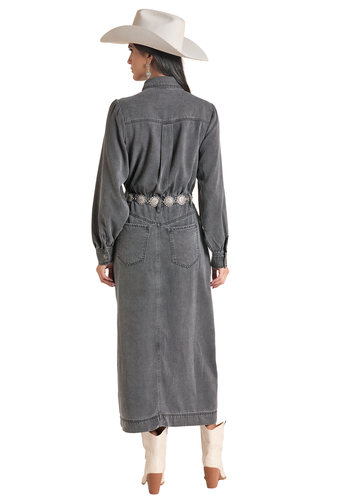 A woman shown from the back wearing a long charcoal gray denim shirt dress with a decorative silver-toned belt, a cream cowboy hat, and cream cowboy boots.