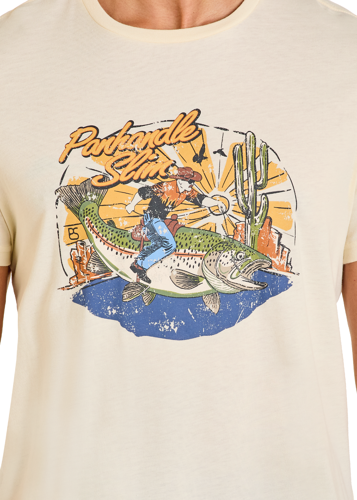 Beige t-shirt with a graphic design of a fish, cactus, and person on a desert landscape.