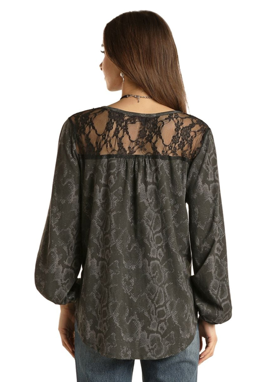 Woman wearing a dark patterned blouse with lace detailing and blue jeans on a white background