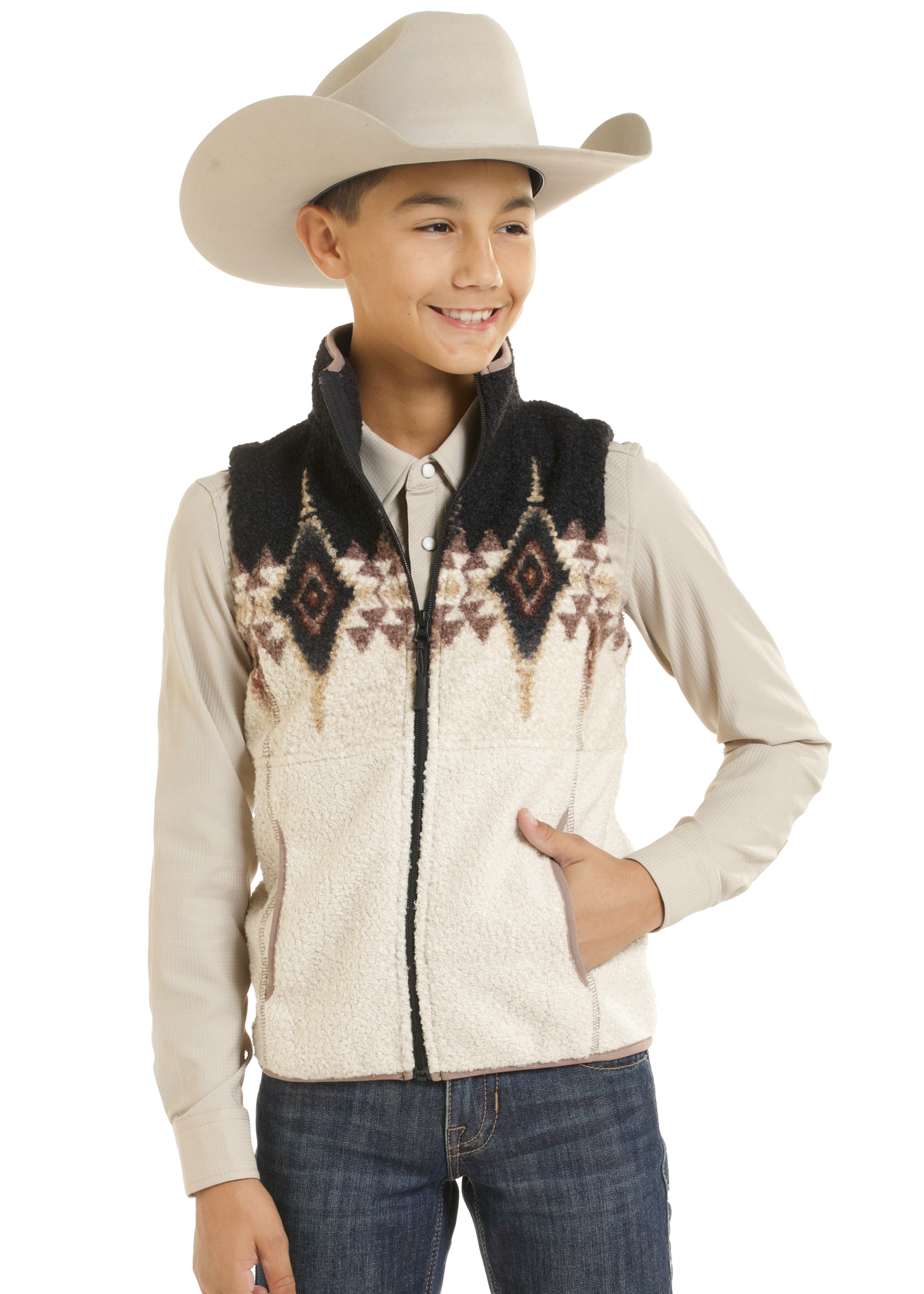 A young boy wearing a cream sherpa fleece vest with a black and brown geometric pattern across the chest, a beige cowboy hat, a light beige long-sleeve shirt, and blue jeans.