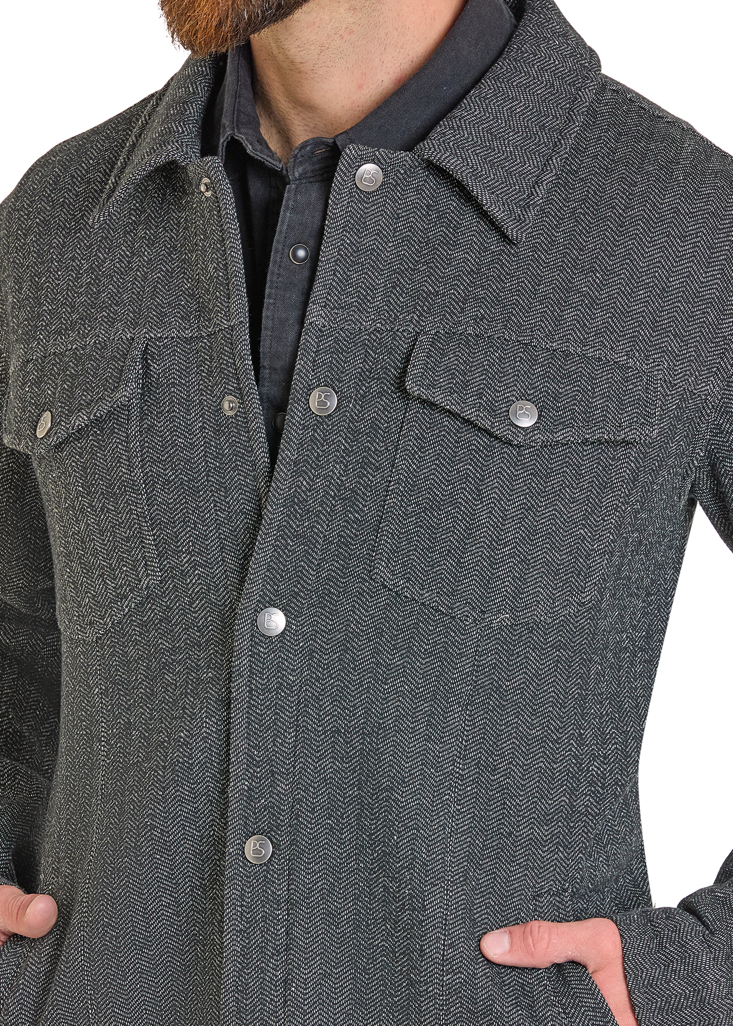 A close-up of a person wearing a dark gray herringbone patterned overshirt with silver buttons over a dark collared shirt.
