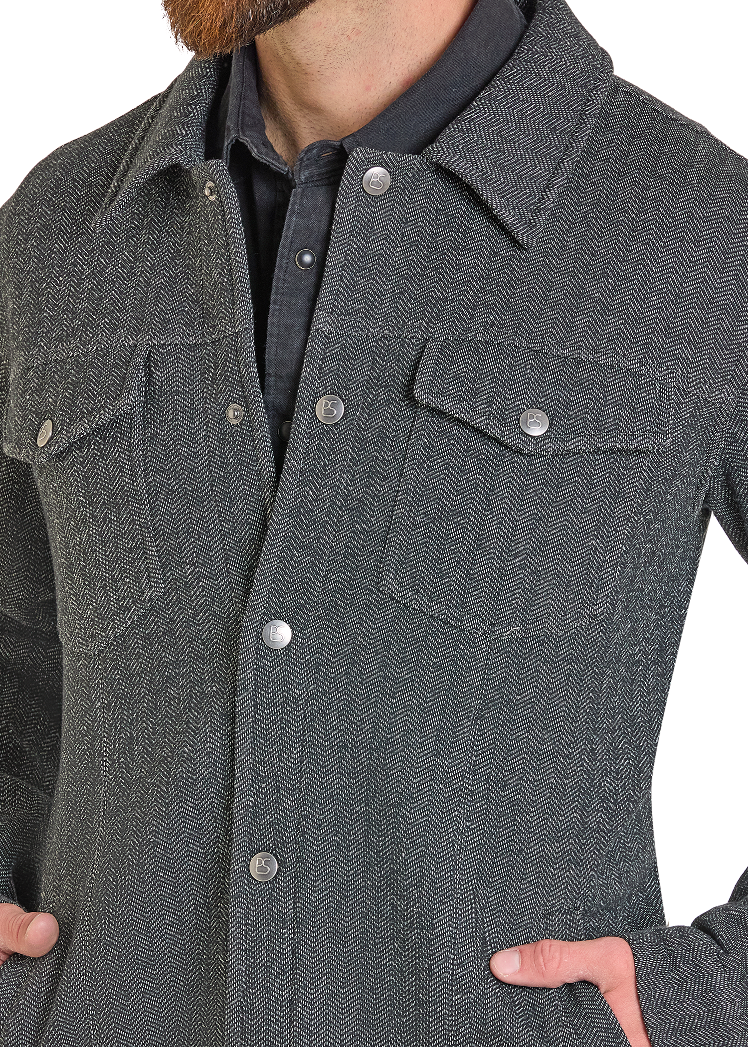 A close-up of a person wearing a dark gray herringbone patterned overshirt with silver buttons over a dark collared shirt.