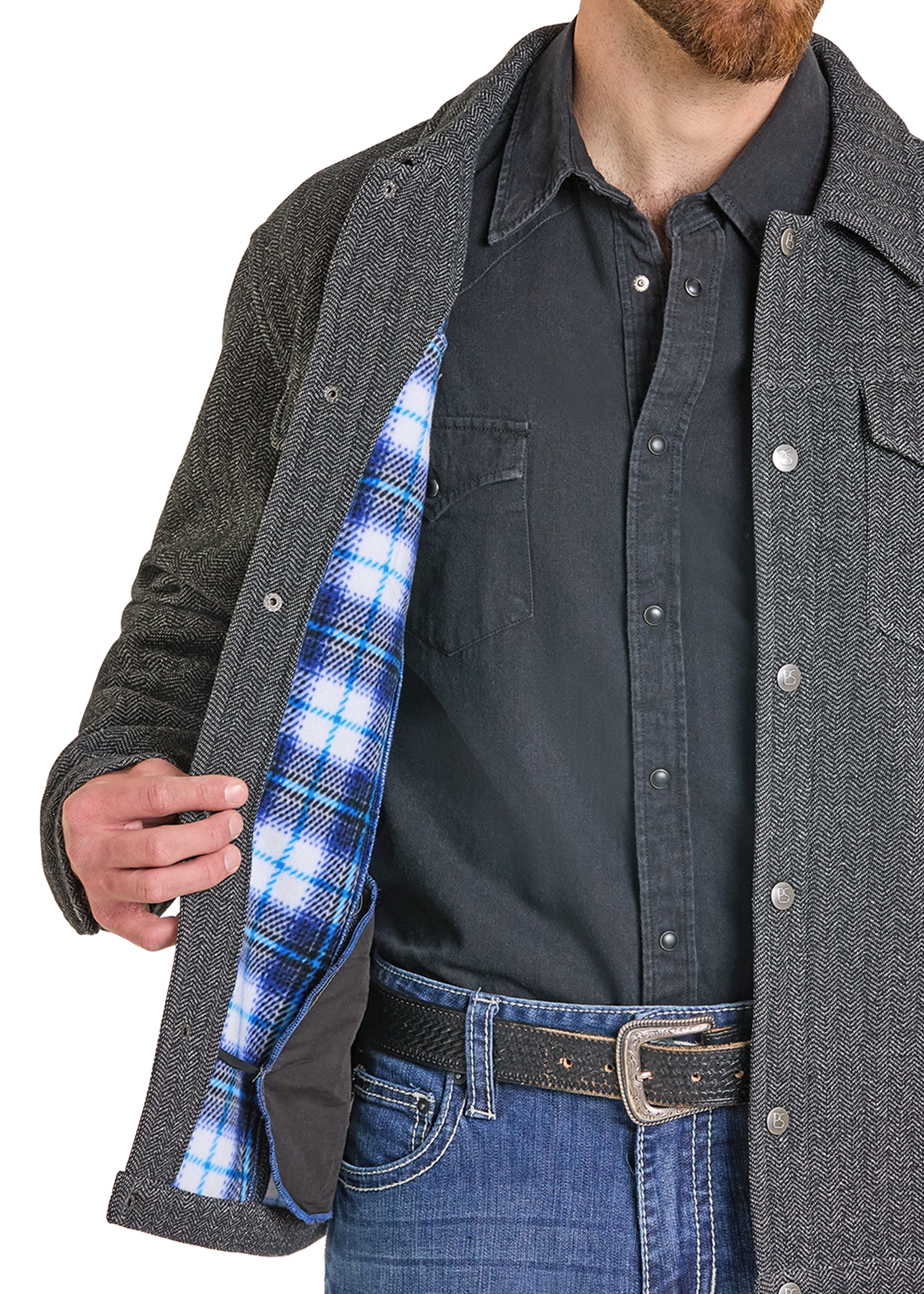 A close-up of a man wearing a dark gray textured overshirt over a black button-up shirt and blue jeans, opening the overshirt to reveal a blue and white plaid lining.