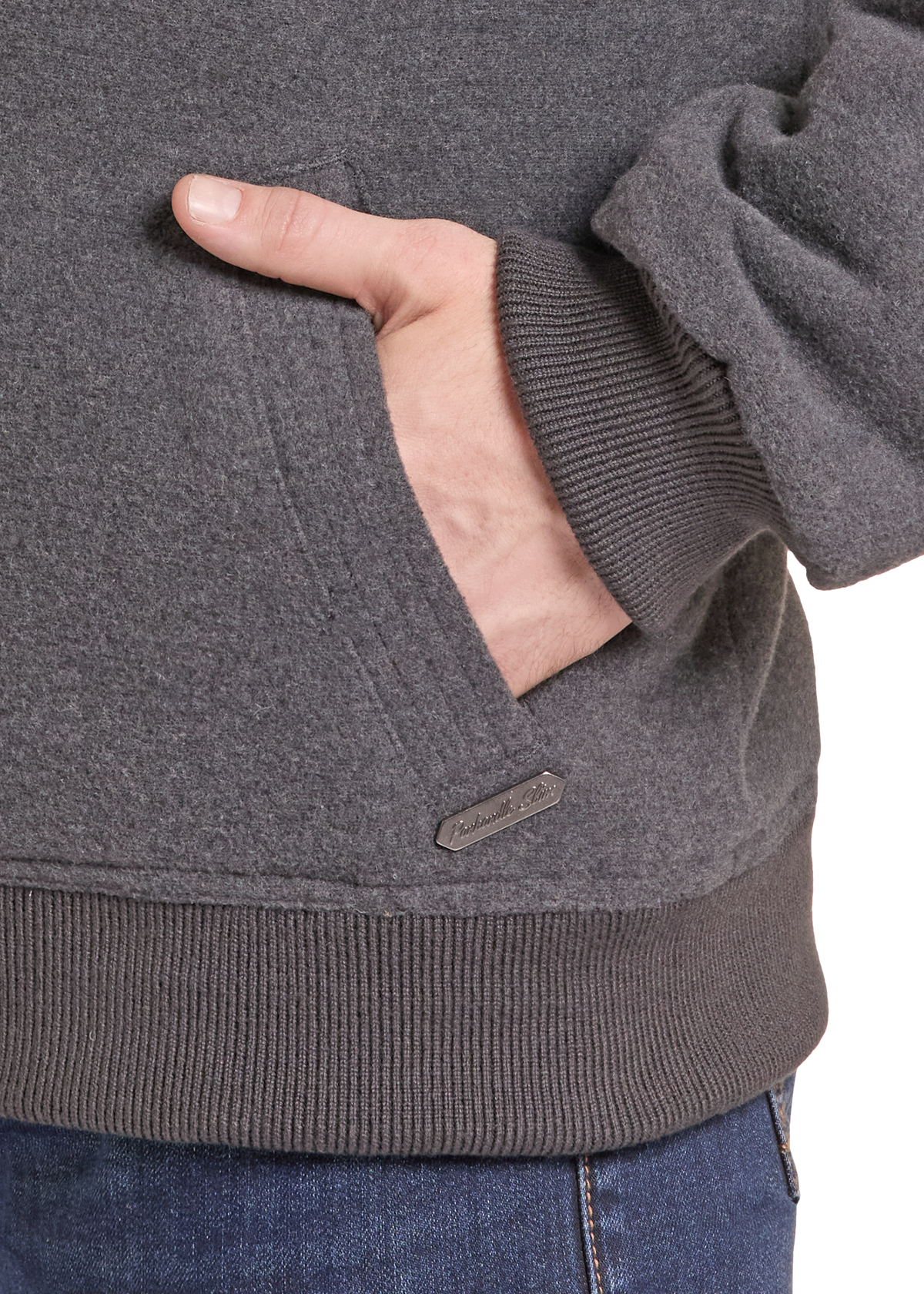 Close-up of a person wearing a dark heather gray pullover hoodie with a ribbed cuff, pocket, and hem, with a small brand tab near the hem.