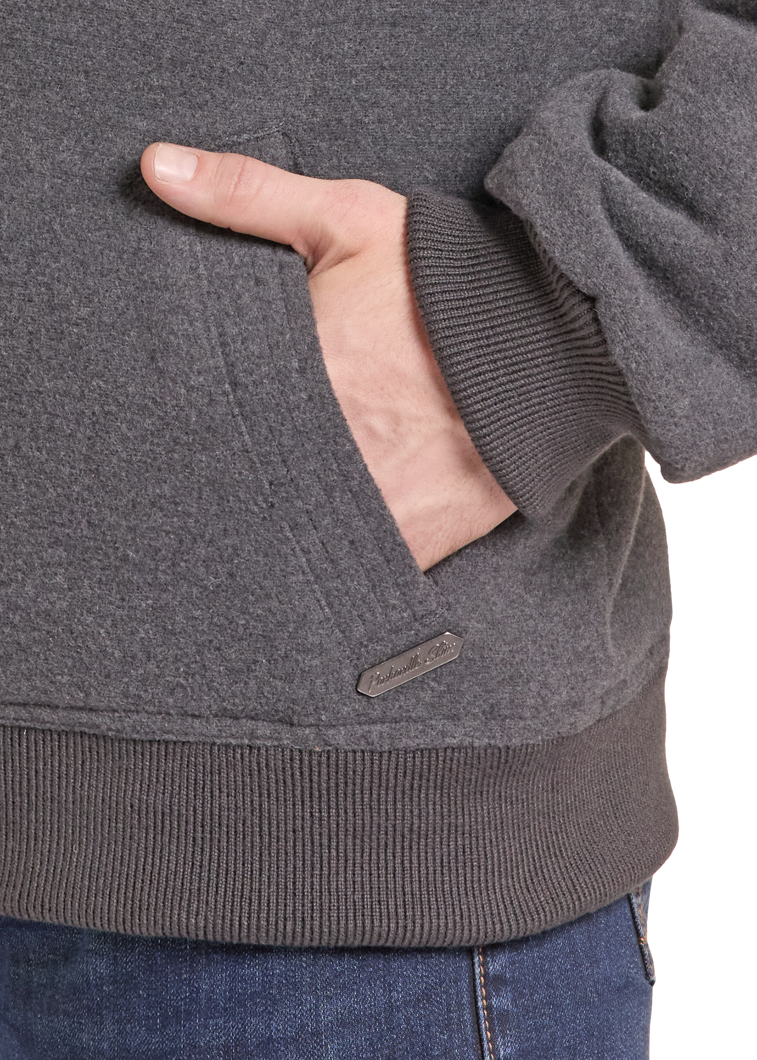 Close-up of a person wearing a dark heather gray pullover hoodie with a ribbed cuff, pocket, and hem, with a small brand tab near the hem.
