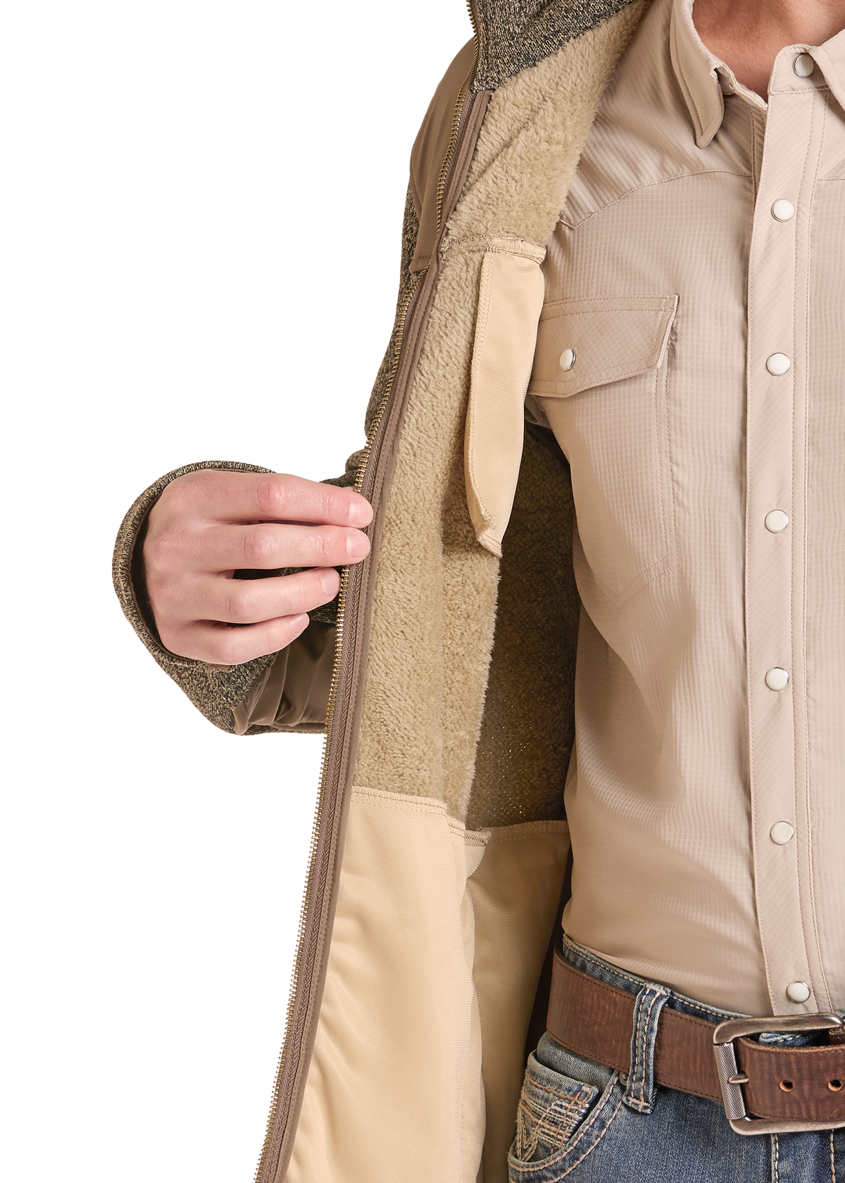 Close-up of a person wearing a tan zip-front jacket with a soft fleece lining, layered over a beige button-up shirt and blue jeans with a brown belt.