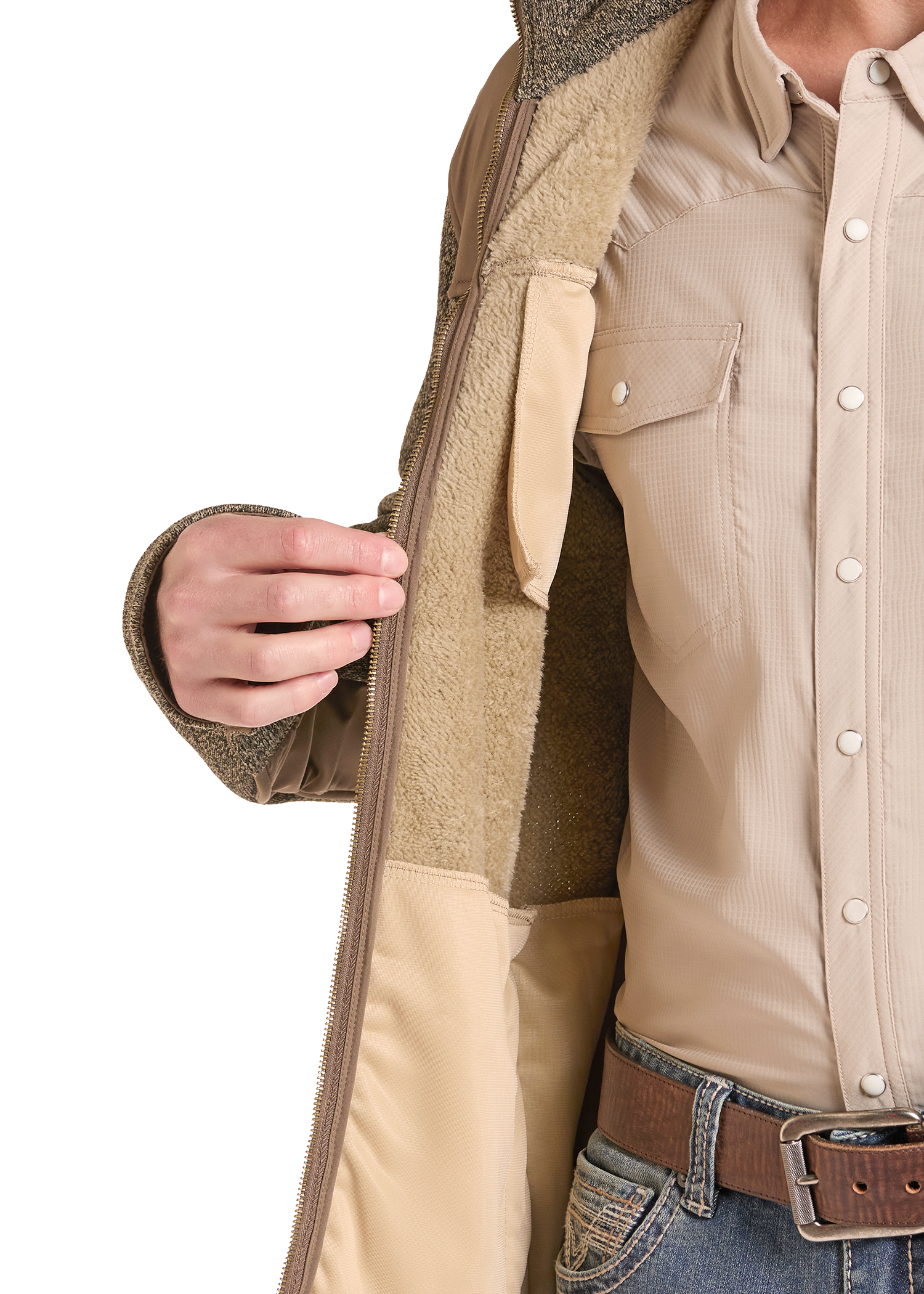 Close-up of a person wearing a tan zip-front jacket with a soft fleece lining, layered over a beige button-up shirt and blue jeans with a brown belt.