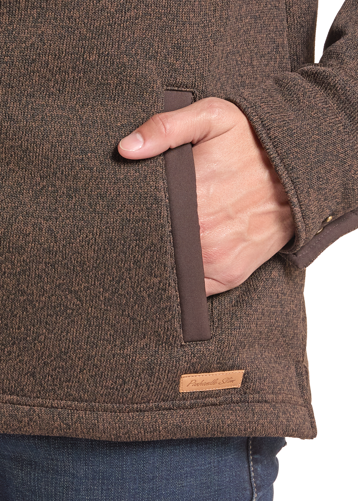 Close-up of a person wearing a brown textured fleece jacket, showing a side pocket with a brown pull tab and a small tan brand label.