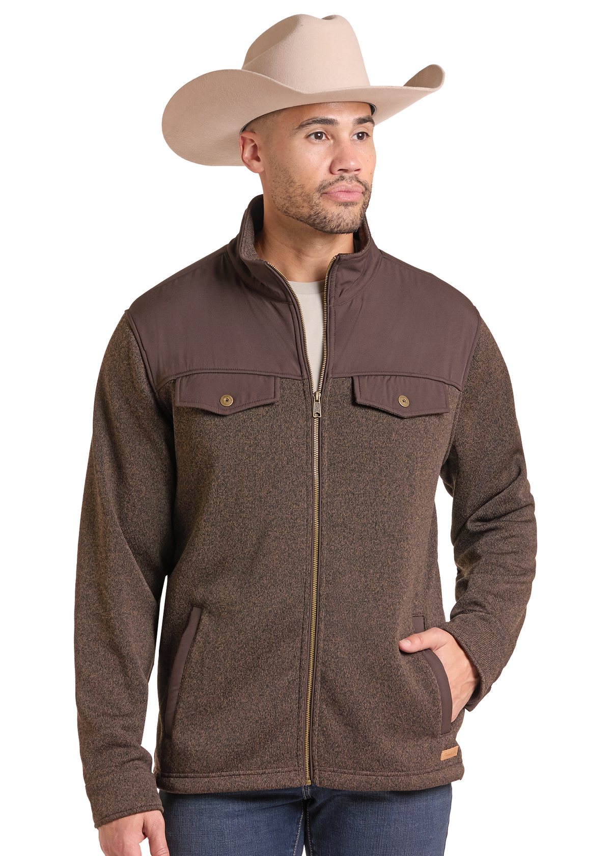 A man wearing a brown zip-up fleece jacket with a stand collar and chest flap pockets, paired with a beige cowboy hat and blue jeans.