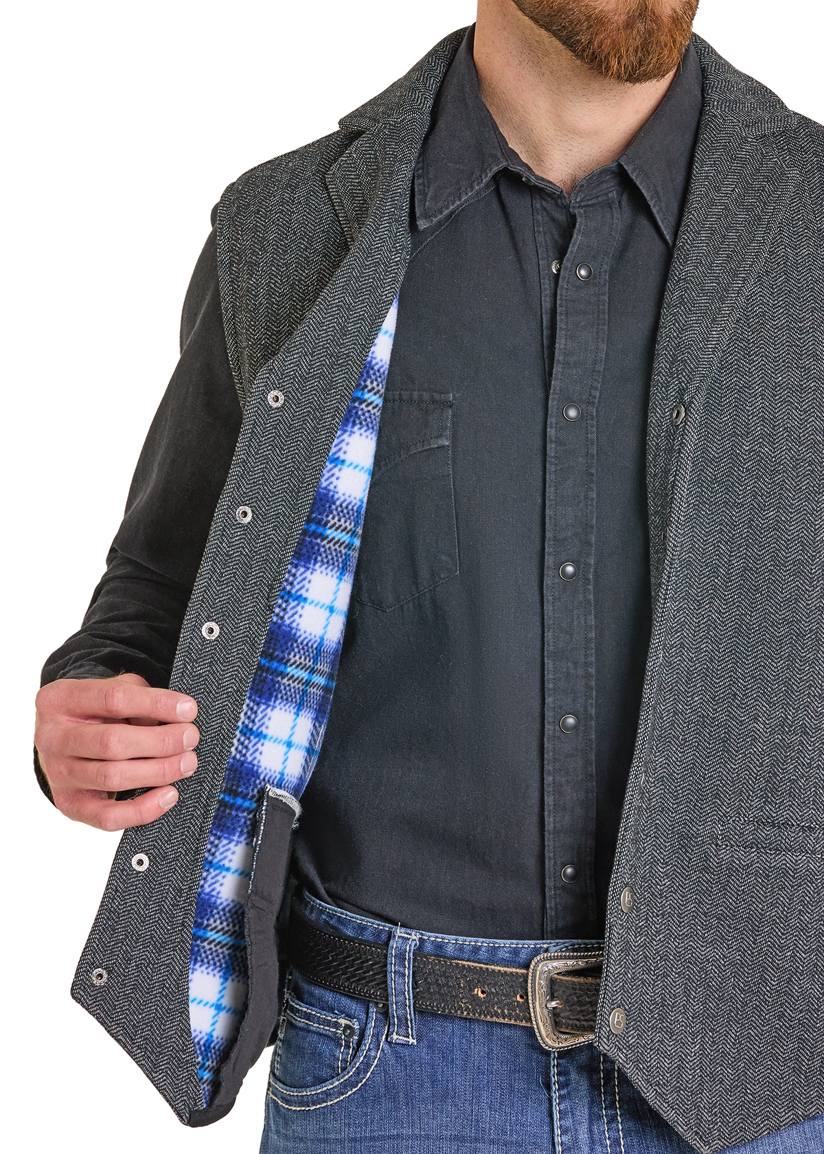A man wearing a dark gray textured overshirt over a black button-up shirt and blue jeans, with the overshirt open to show a blue and white plaid lining.