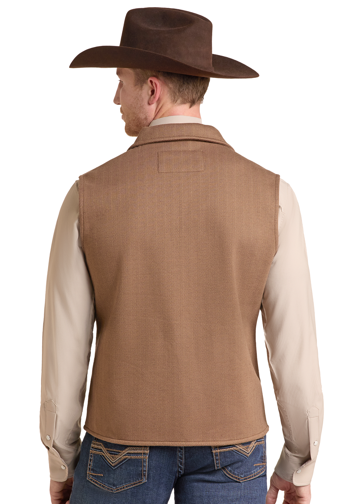 A man shown from the back wearing a brown cowboy hat, a tan sleeveless vest over a light beige long-sleeve shirt, and blue jeans.