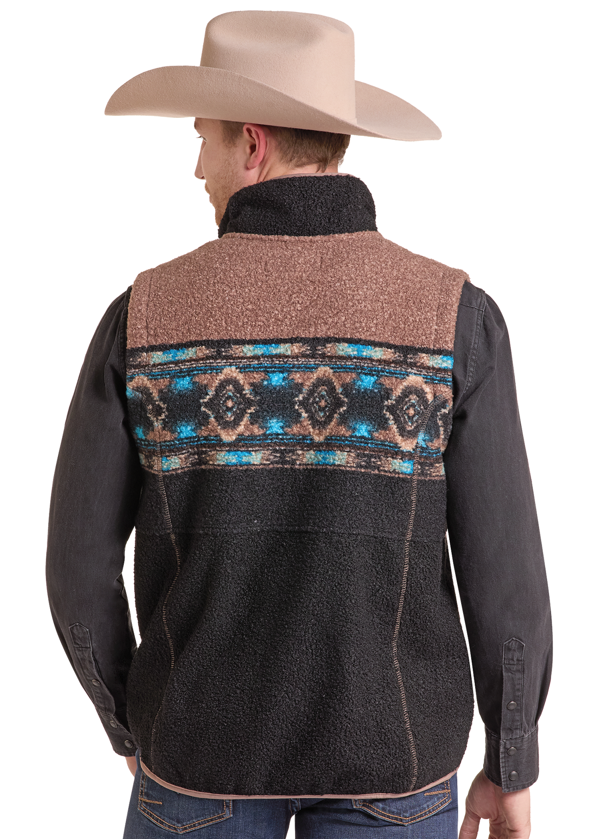 A man wearing a brown and black fleece vest with a colorful Southwestern-style geometric pattern across the upper back, paired with a tan cowboy hat, dark long-sleeve shirt, and jeans.