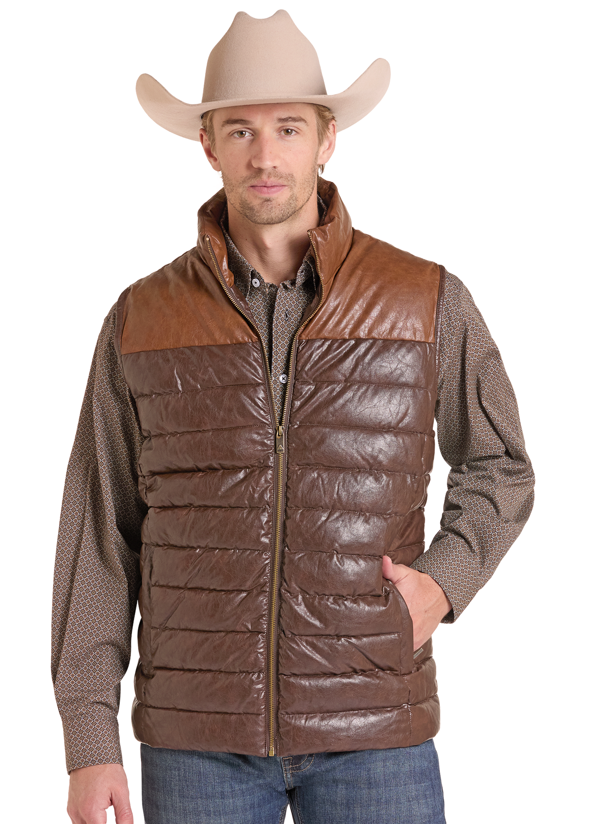 A man wearing a brown quilted puffer vest with a smooth brown faux-leather yoke, styled with a brown patterned shirt, blue jeans, and a beige cowboy hat.