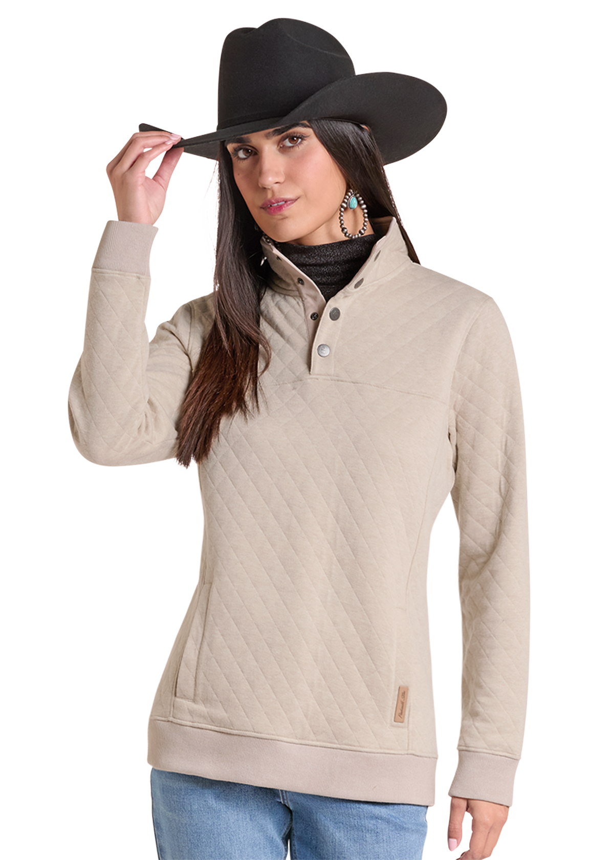 A woman wearing a beige quilted long-sleeve half-placket pullover with a stand collar, styled with a black cowboy hat, a black turtleneck, and blue jeans.