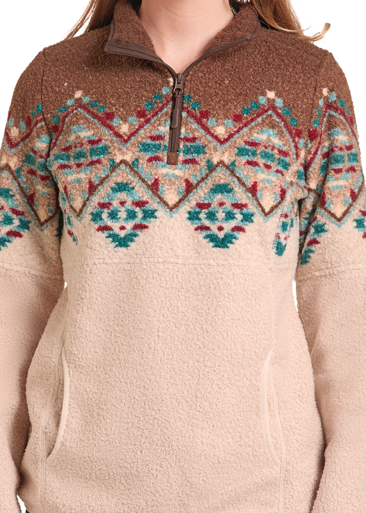 A close-up of a person wearing a quarter-zip fleece pullover sweater. The top portion is brown with a colorful geometric Fair Isle pattern in teal, red, and cream, while the lower portion is solid cream.