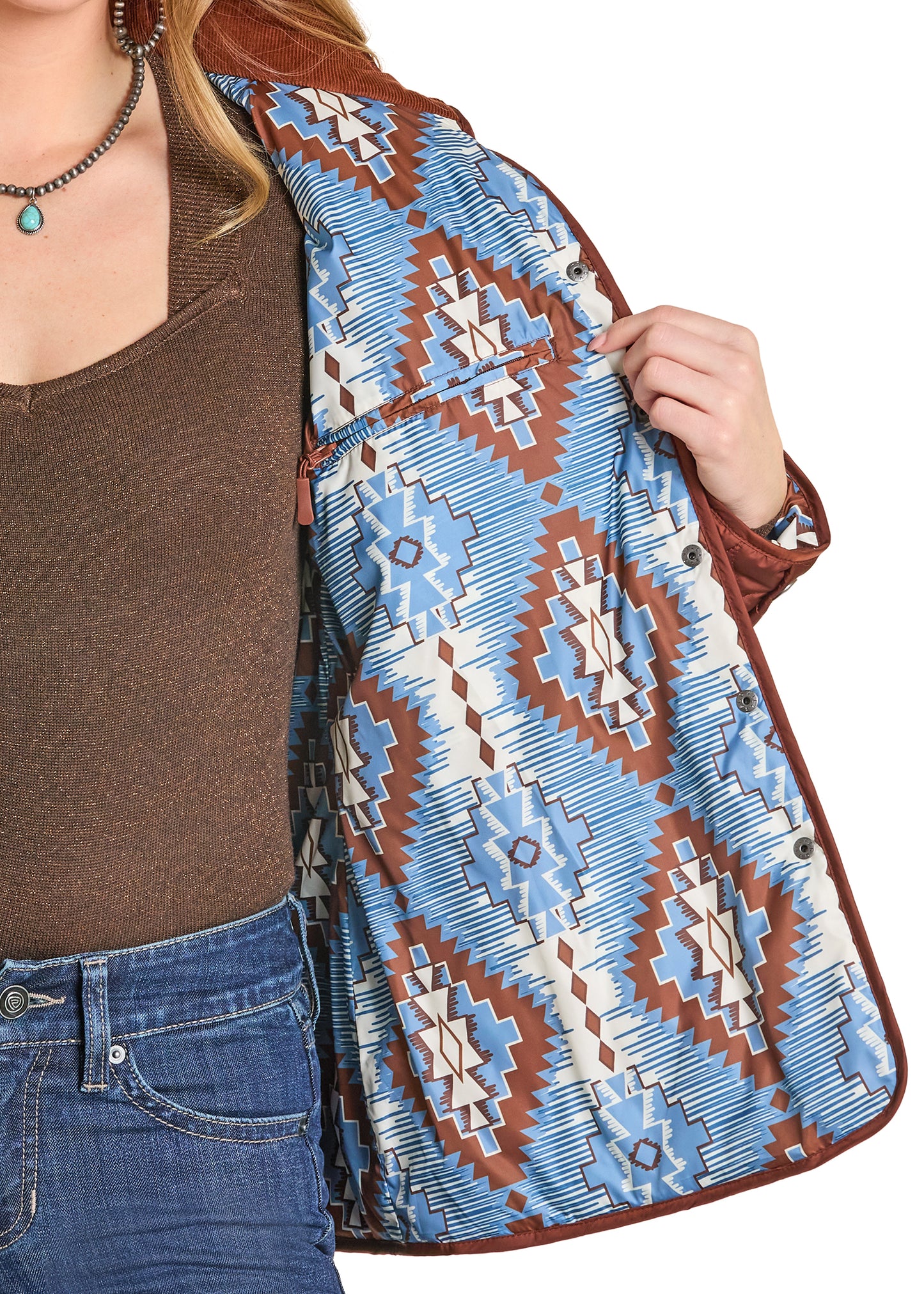 Person wearing a patterned jacket with a brown shirt and blue jeans on a white background