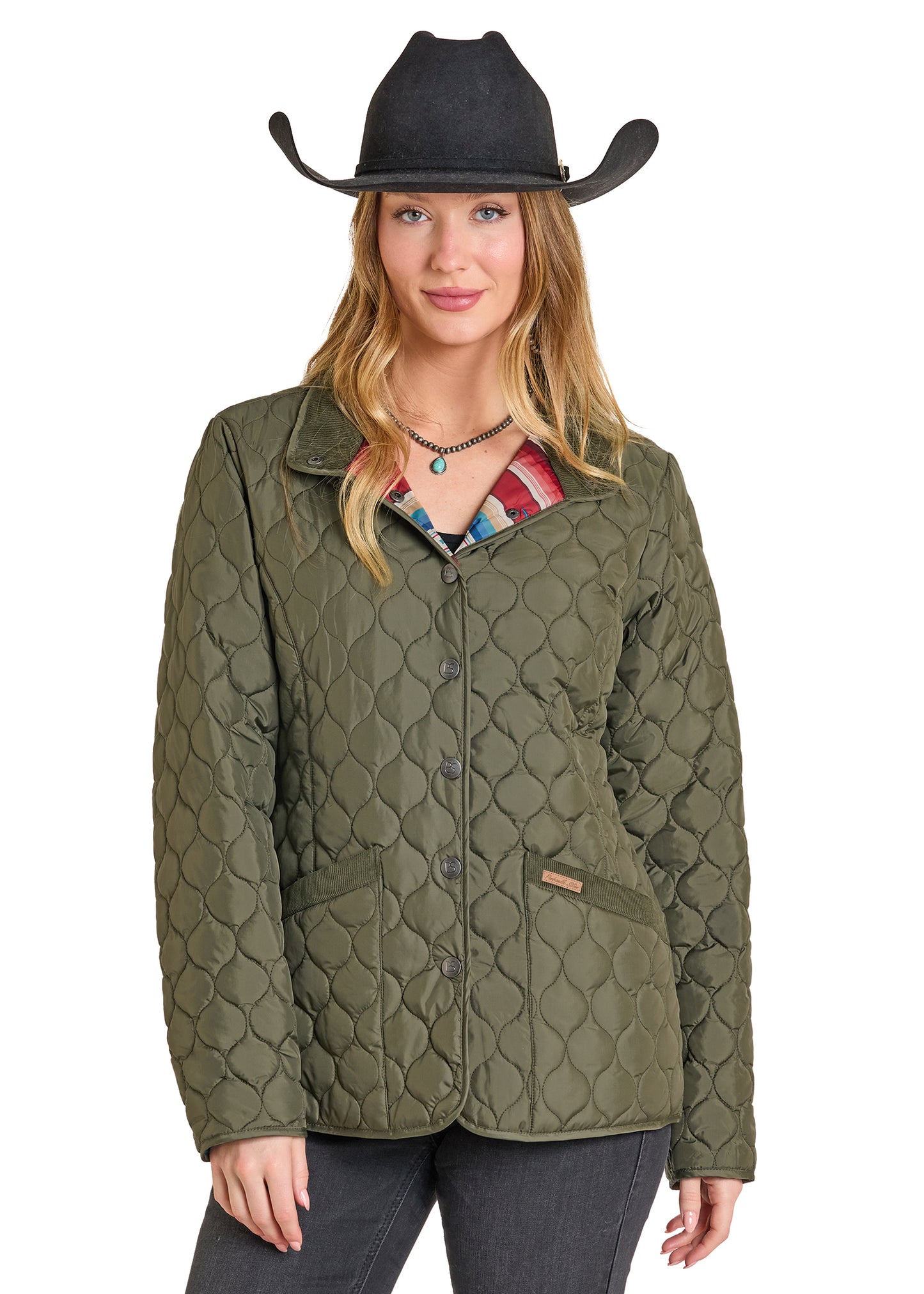Woman wearing a quilted green jacket and black cowboy hat on a white background
