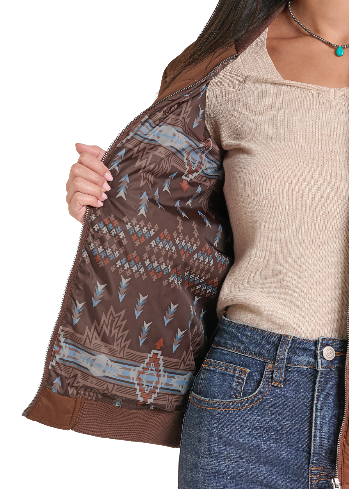 A close-up of a person wearing a brown patterned bomber jacket, showing the interior lining with a Southwestern-style geometric print in brown, beige, and blue. 