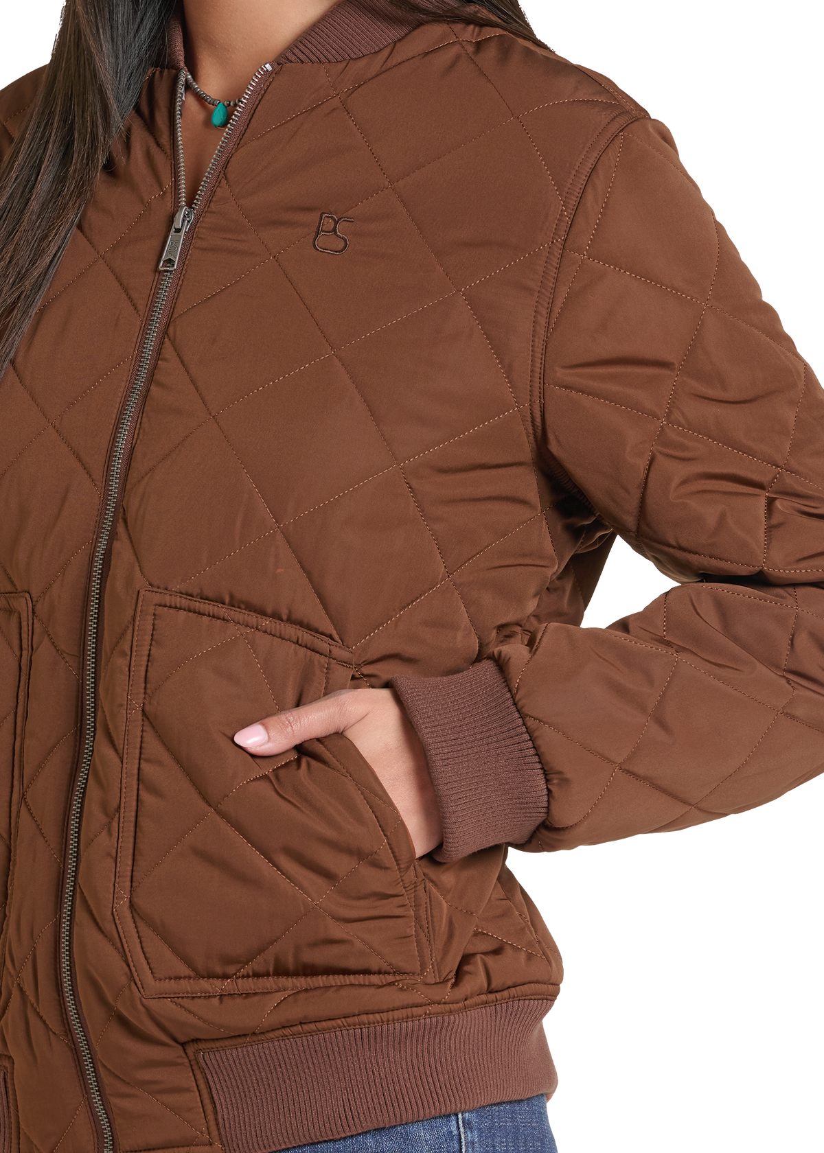 A close-up of a person wearing a brown diamond-quilted zip-front jacket with ribbed collar, cuffs, and hem, plus a small embroidered chest logo.