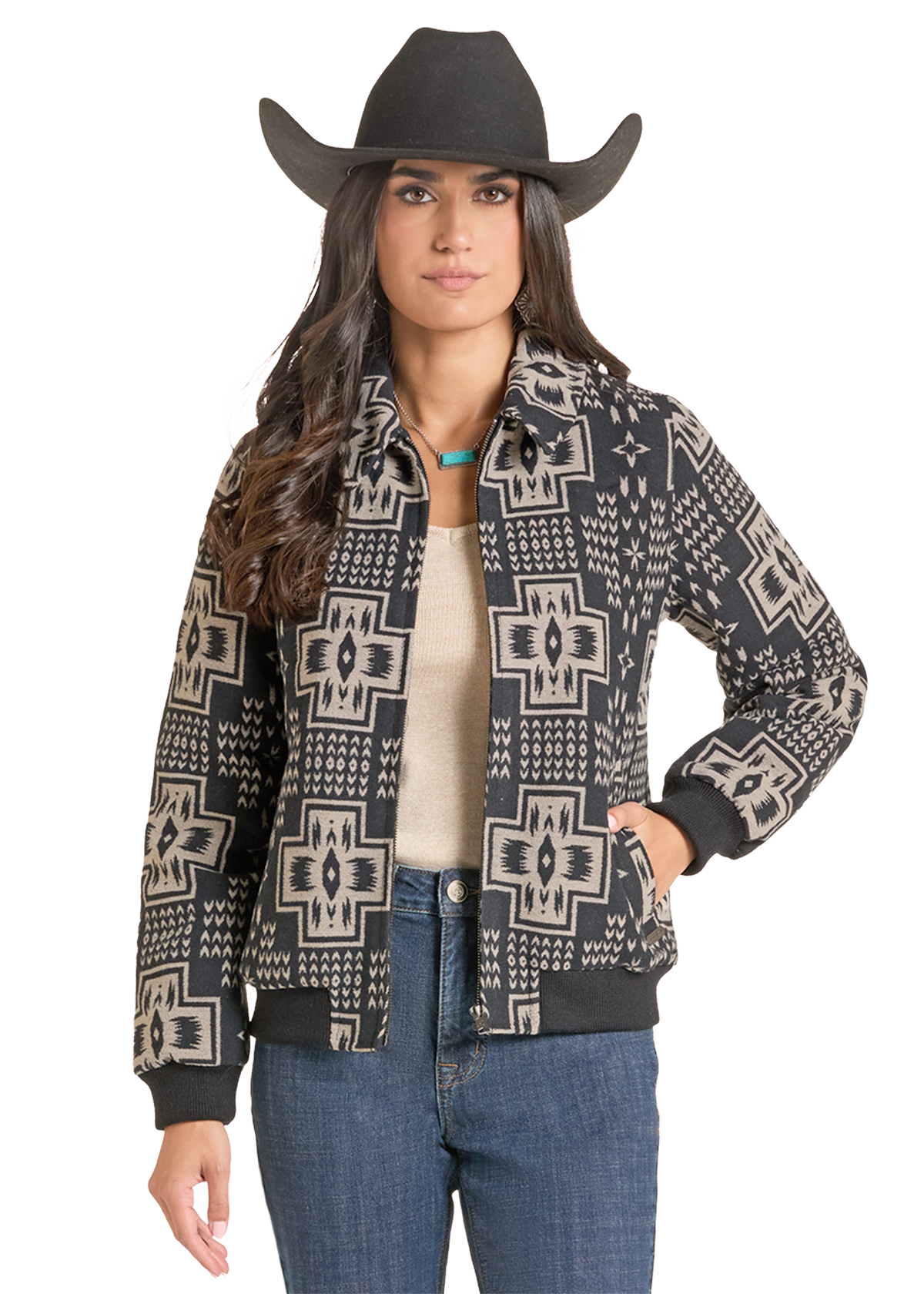 A woman modeling a black and beige southwestern patterned bomber jacket, paired with a black cowboy hat, beige top, and blue jeans.