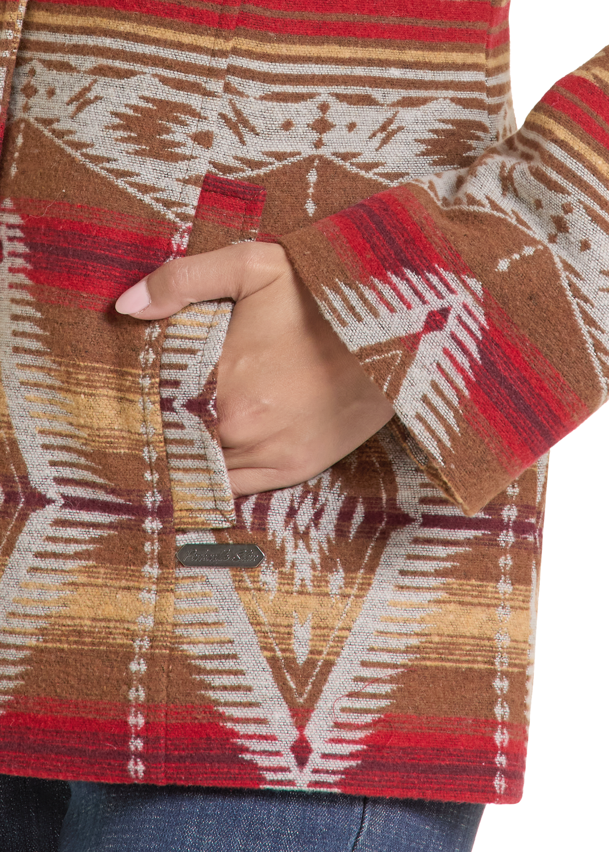 Close-up of a person wearing a patterned  jacket with a hand tucked into the front pocket. The jacket features a Southwestern geometric pattern in brown, red, beige, and white.