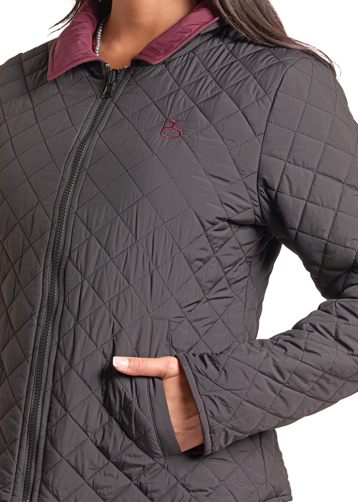 Detail image of Woman wearing a black quilted zip up jacket with her hand in her pocket.