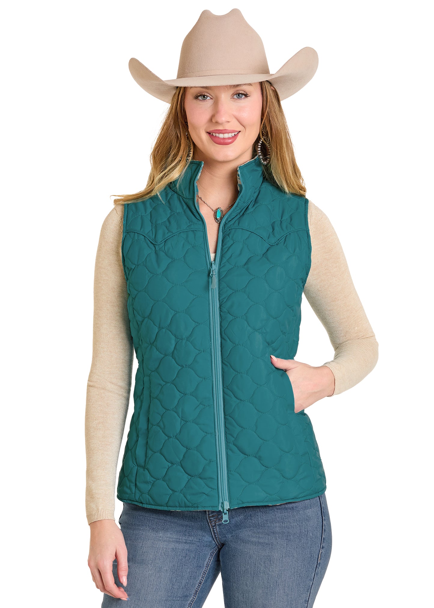 Woman wearing a teal quilted vest, beige long-sleeve shirt, jeans, and a beige cowboy hat on a white background.