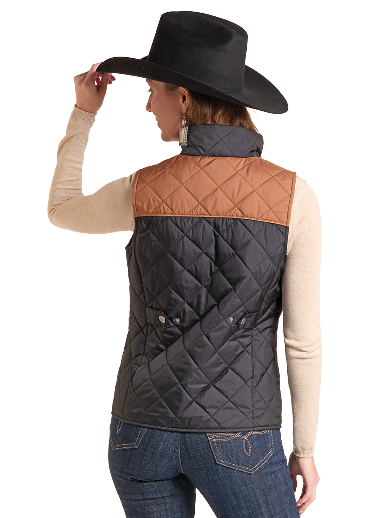 A woman shown from the back wearing a quilted sleeveless puffer vest with a black body and a tan yoke, styled with a black cowboy hat, beige long-sleeve top.