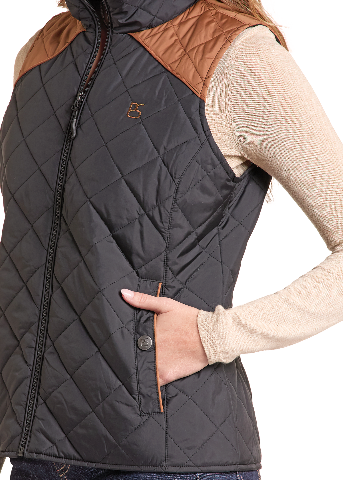 A close-up of a woman wearing a sleeveless quilted vest with brown shoulder panels and a small embroidered logo on the chest.