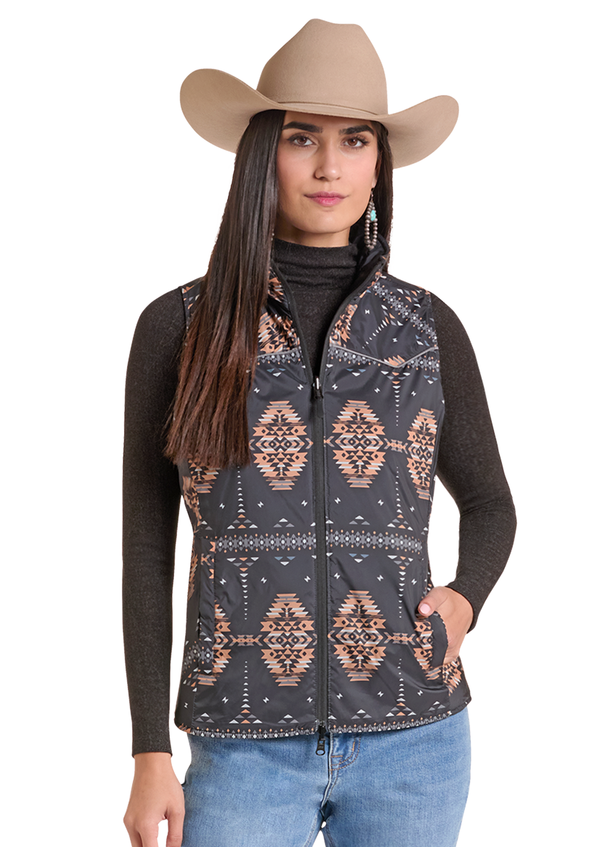 A woman wearing a sleeveless zip-front vest with a dark gray and black base and a geometric southwestern pattern in beige and brown, styled with a tan cowboy hat, dark long-sleeve top, and blue jeans.