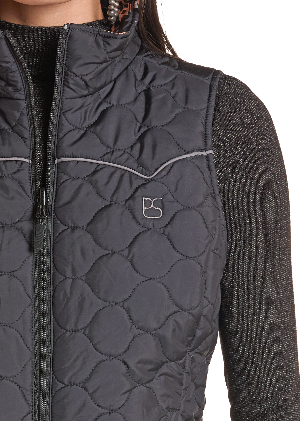 Close-up of a dark gray quilted zip-front vest worn over a dark heathered knit sweater. The vest has a stand collar, a front zipper, a zip chest pocket, and a small embroidered logo on the left chest.