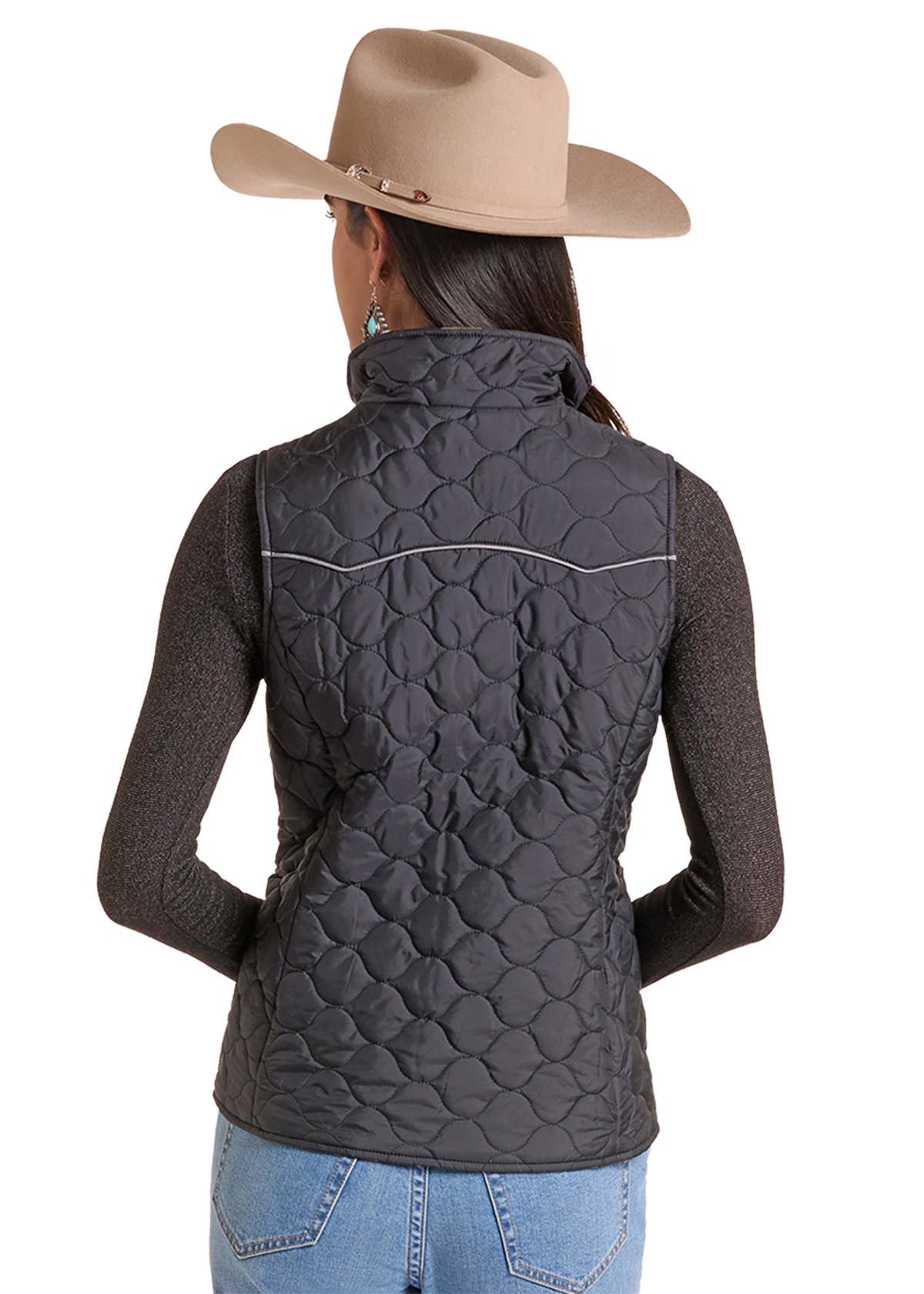 A woman shown from the back wearing a dark gray quilted vest over a dark gray long-sleeve top, blue jeans, and a beige cowboy hat.