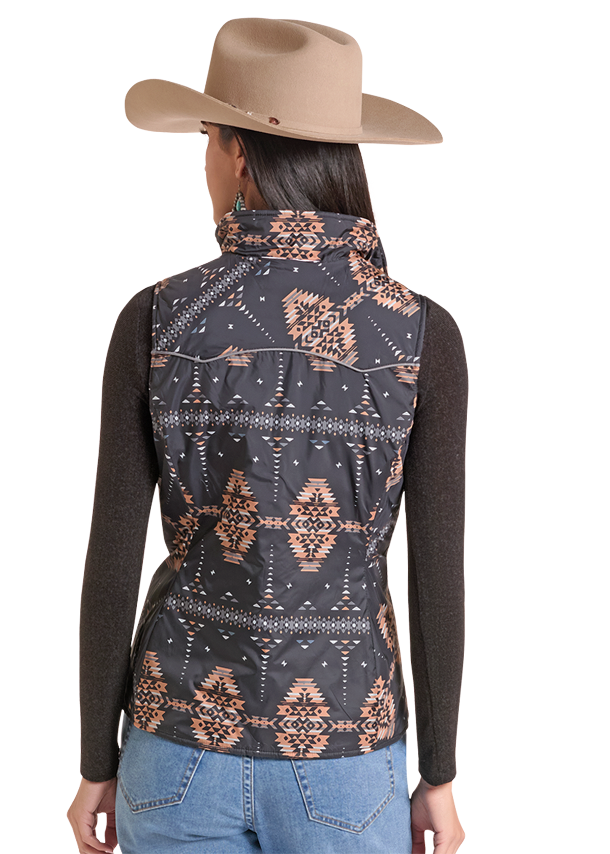 A woman shown from the back wearing a sleeveless patterned vest over a dark long-sleeve top, with a tan cowboy hat and blue jeans.