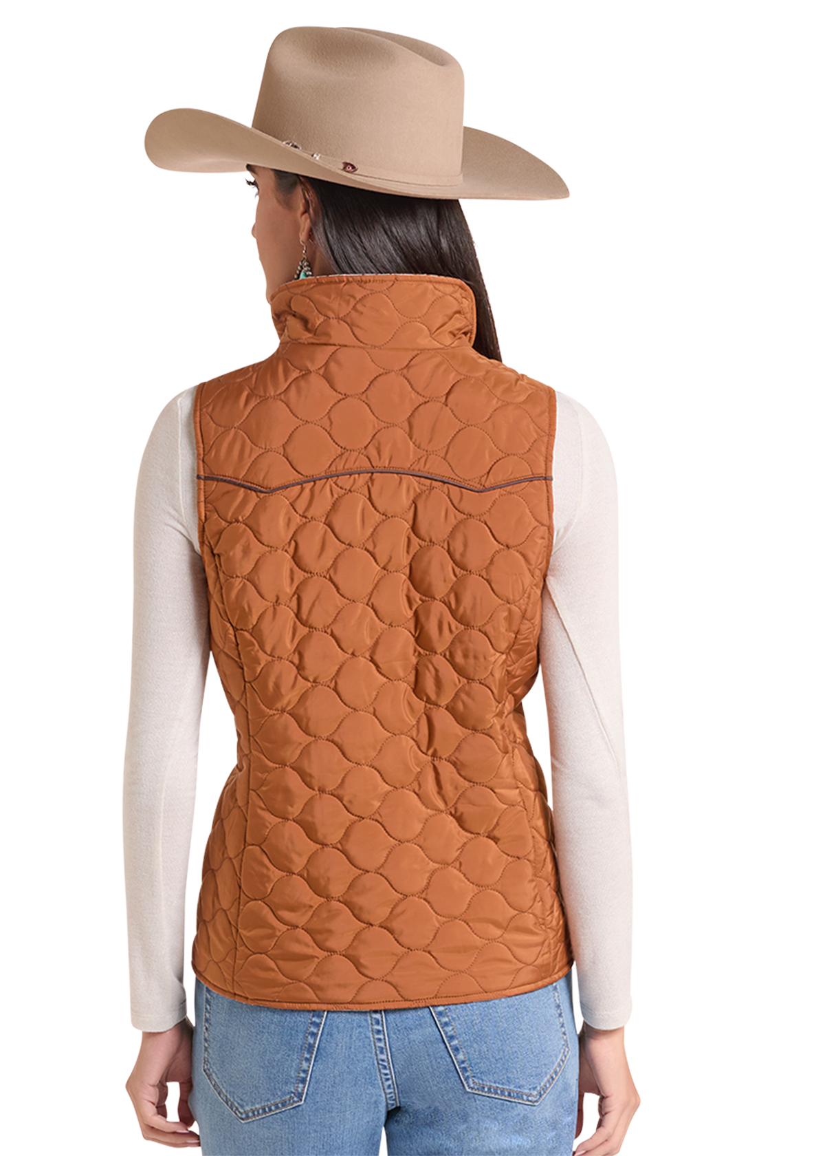 A woman shown from the back wearing a tan cowboy hat, a rust-orange quilted puffer vest over a cream long-sleeve shirt, and blue jeans.