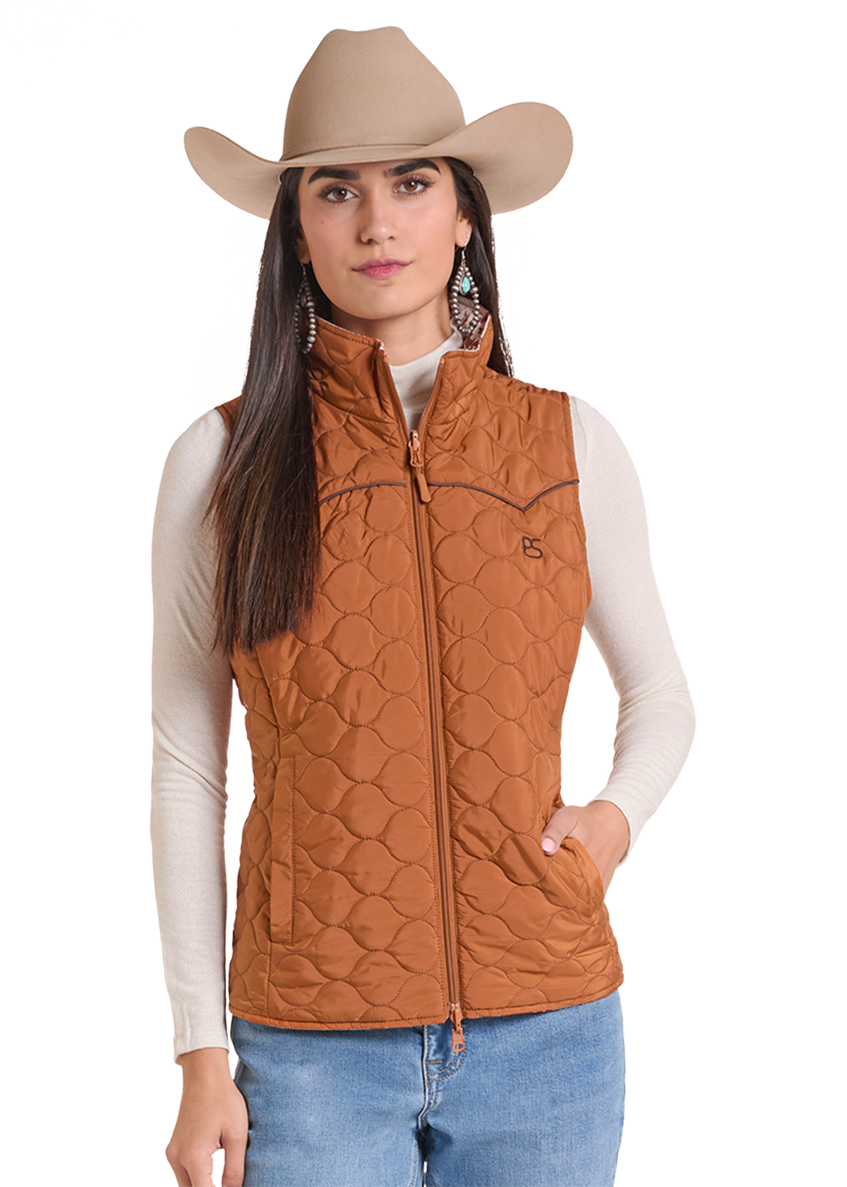 A woman wearing a tan cowboy hat, a rust-brown quilted sleeveless vest over a cream long-sleeve shirt, and blue jeans.