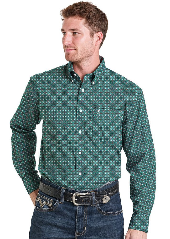 A man wearing a green long-sleeve button-down shirt with a small white geometric pattern, paired with dark blue jeans and a black belt.