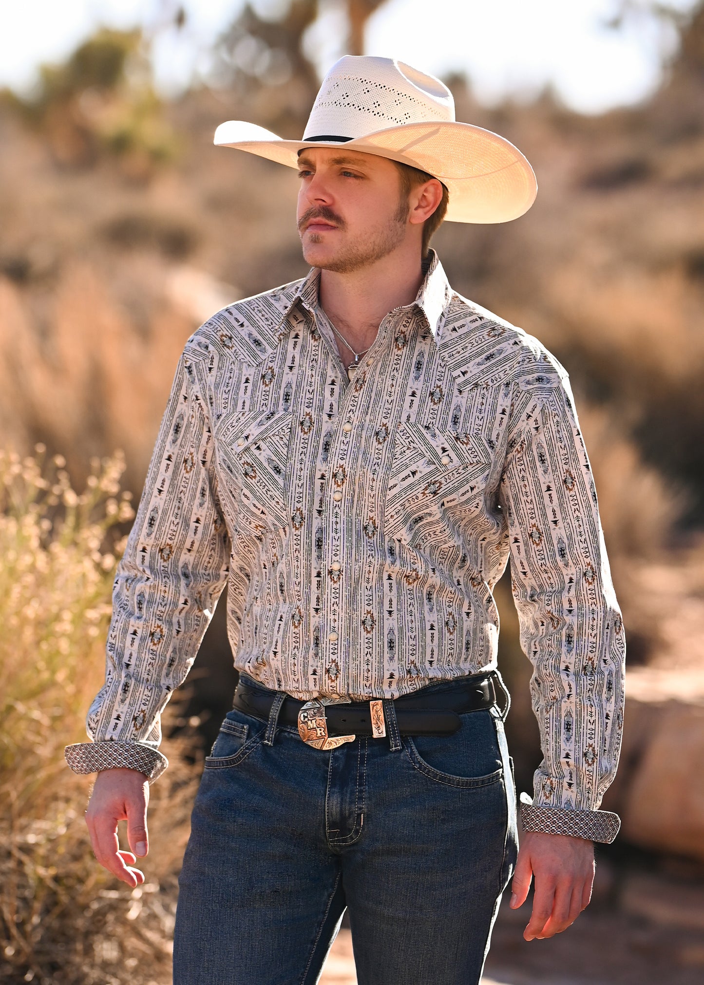 Man wearing a patterned shirt and cowboy hat in a Western, desert setting
