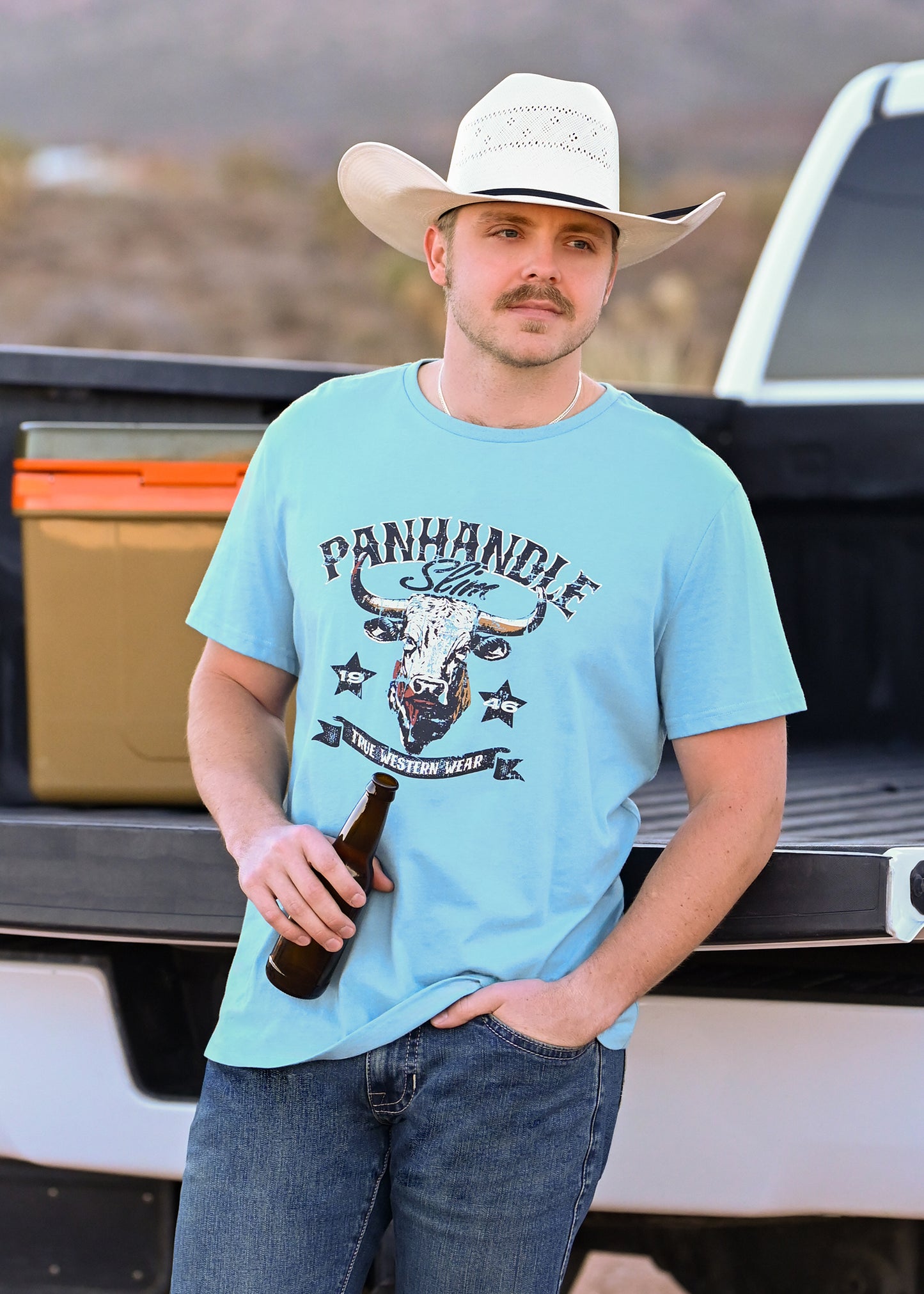 Man wearing a light blue t-shirt with a graphic design, standing in front of a pickup truck.