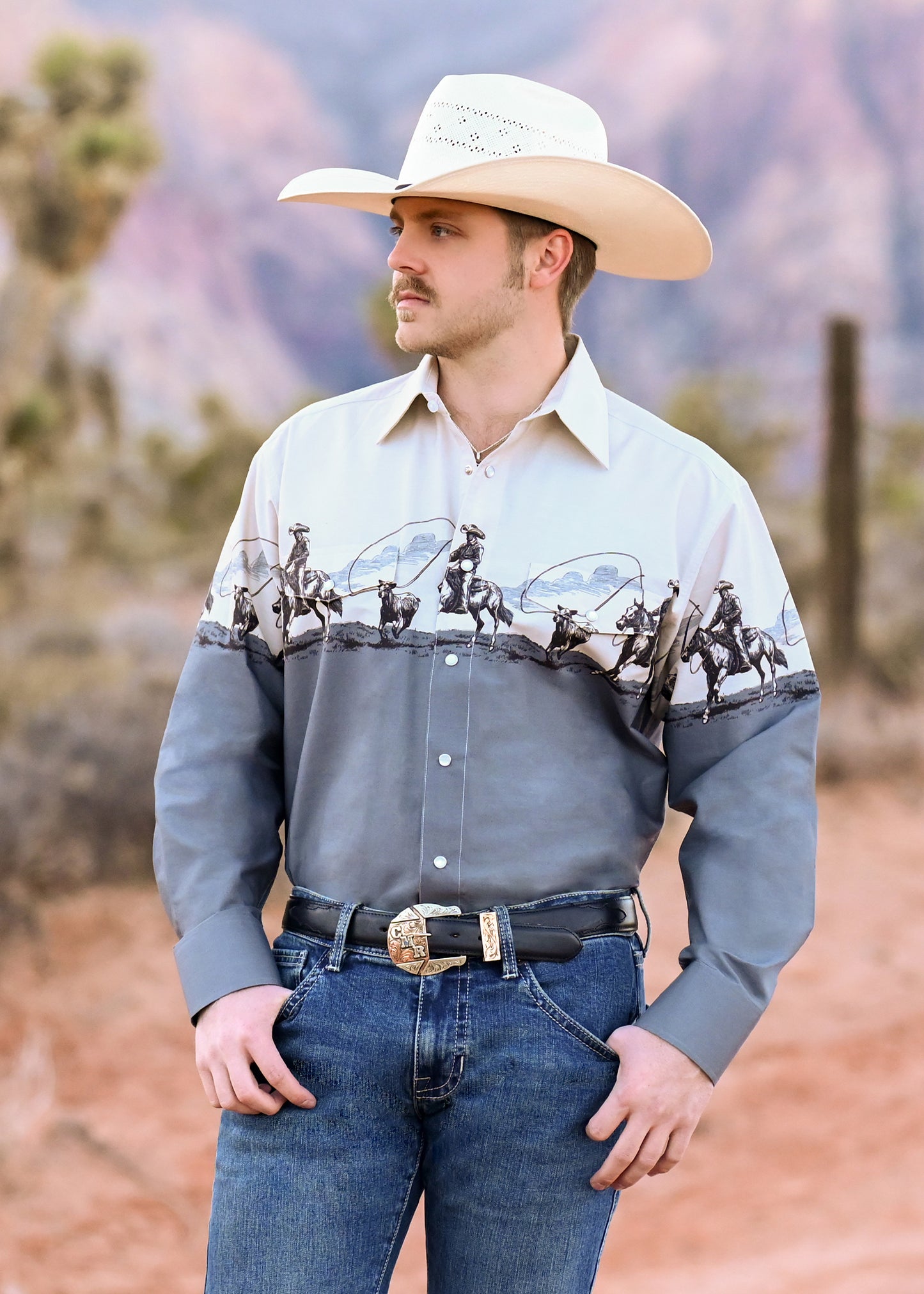 Cowboy wearing a snap shirt with a western roping print in a desert setting. 