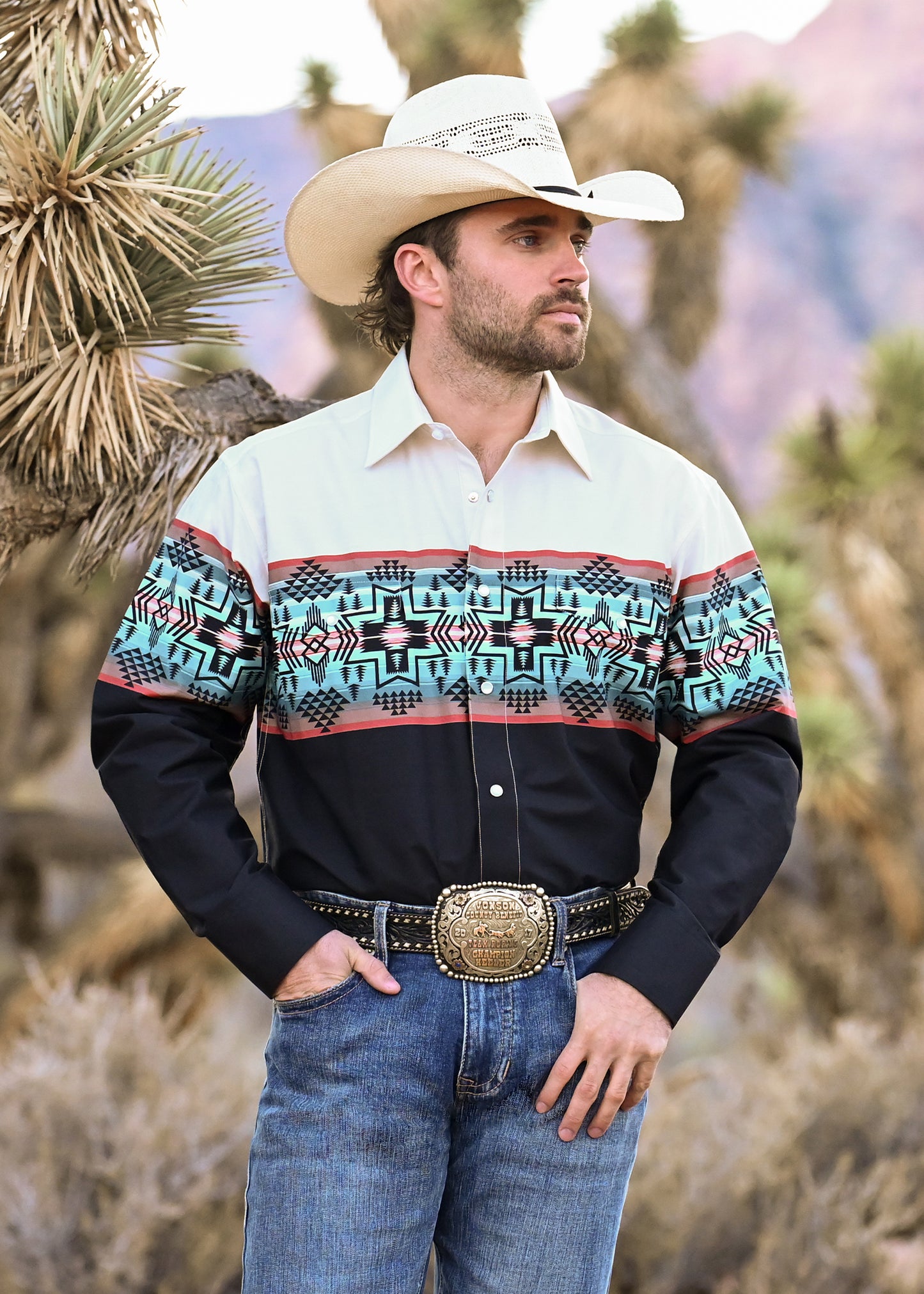 Man wearing a patterned shirt and cowboy hat in a desert setting