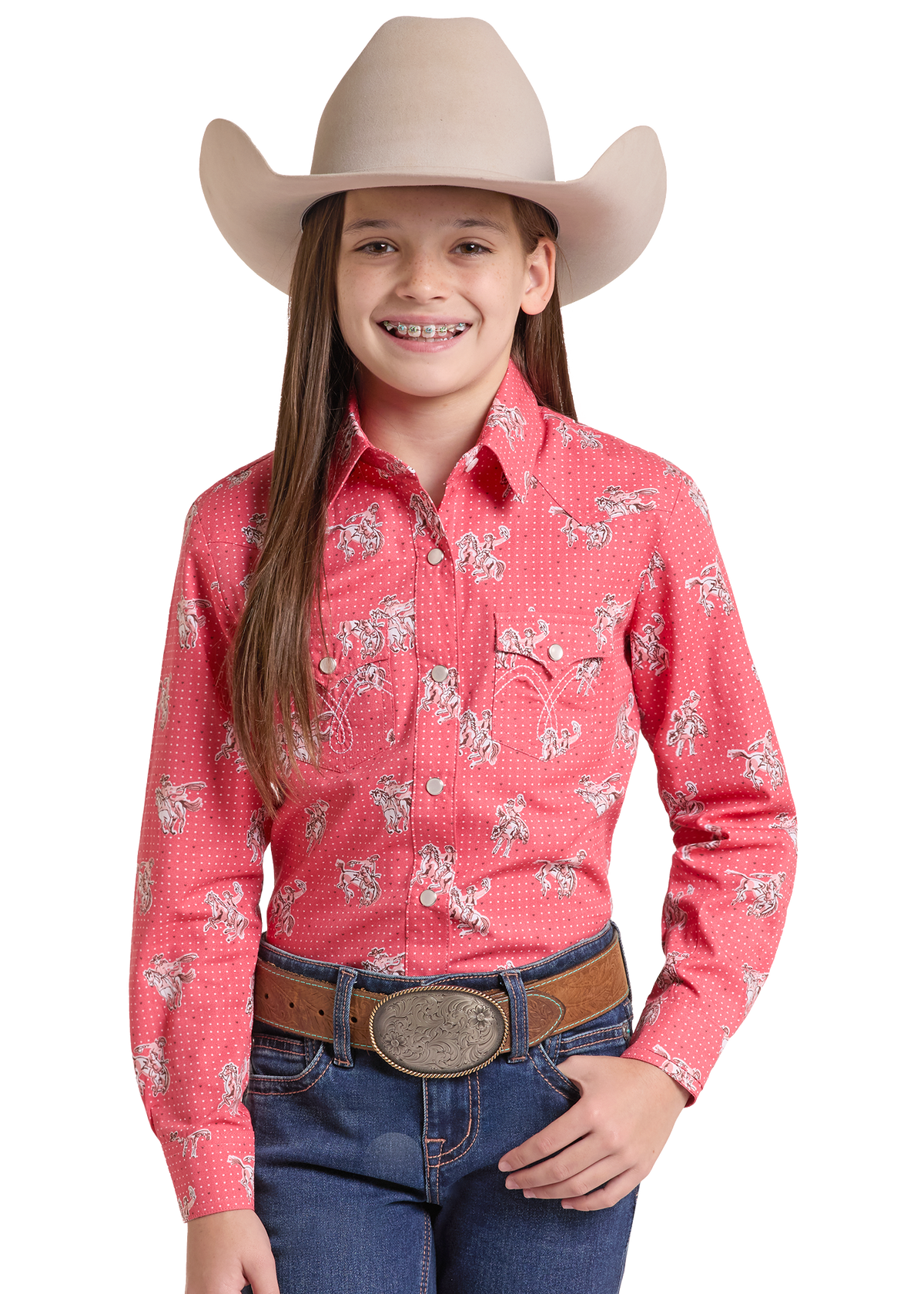 A young girl with long brown hair and braces wearing a pink western long-sleeve shirt with a white cowboy horse pattern, blue jeans, a brown leather belt, and a beige cowboy hat.