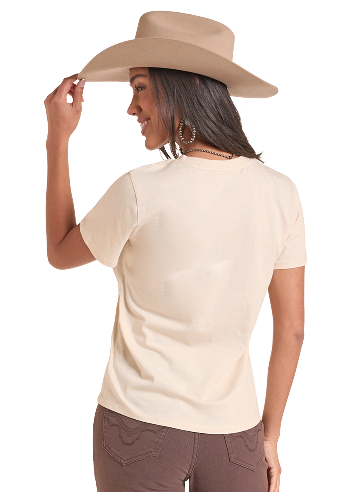 A woman shown from the back wearing a light beige short-sleeve crewneck t-shirt, a tan cowboy hat, and brown pants.