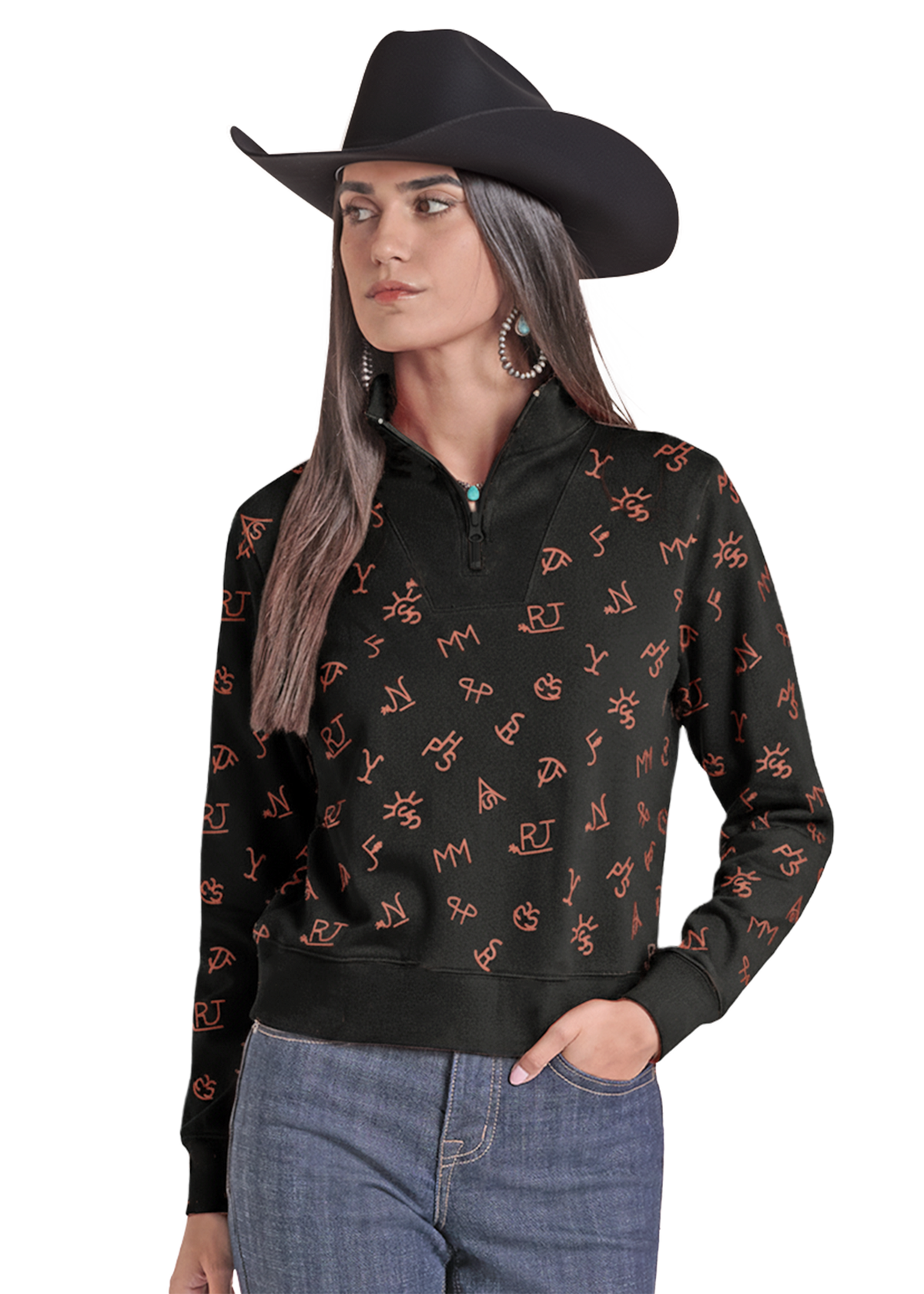 A woman wearing a black cowboy hat, a black quarter-zip sweatshirt with an orange western monogram pattern, and blue jeans.