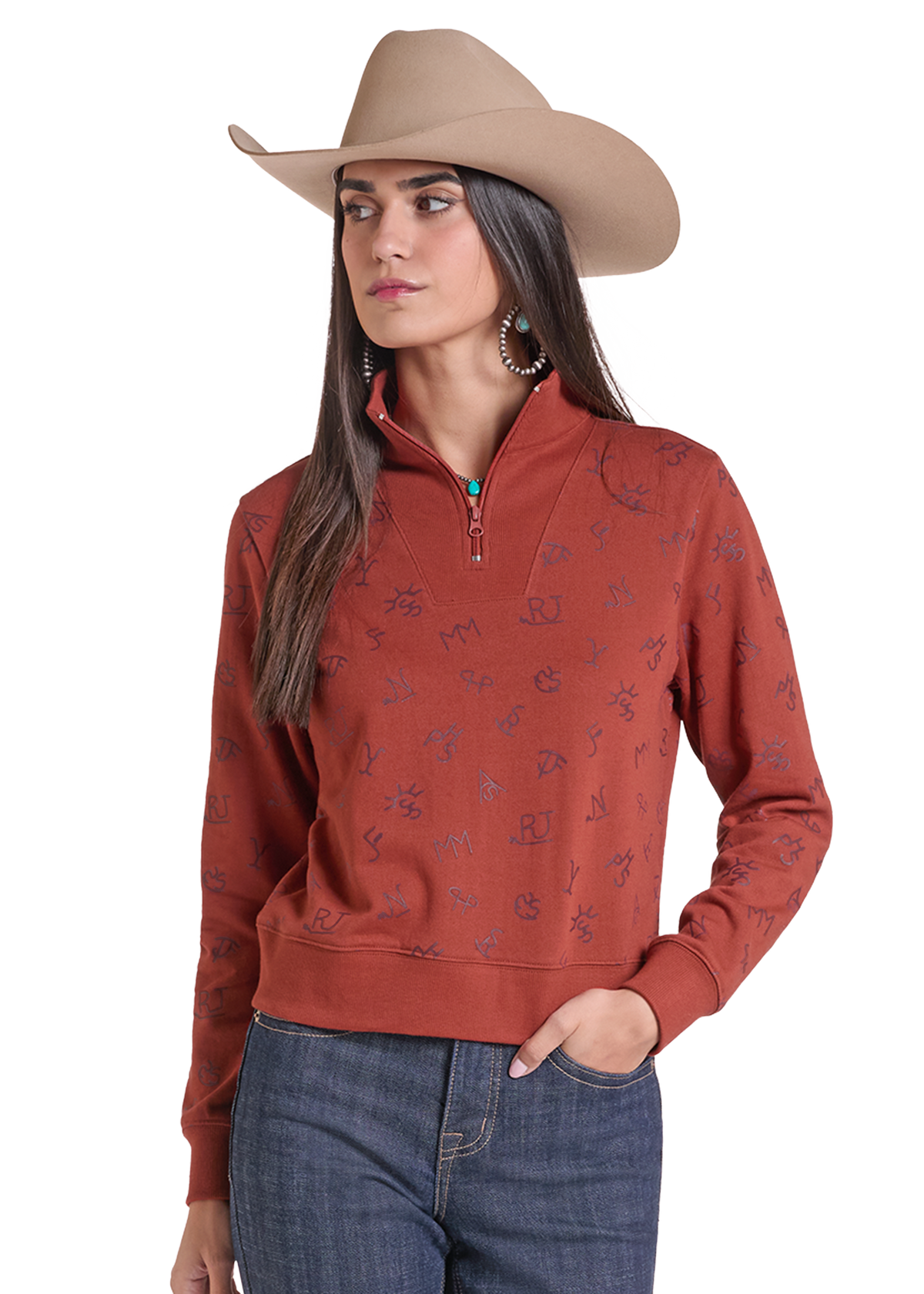 A woman wearing a rust-colored quarter-zip sweatshirt with a subtle tonal floral pattern, paired with a tan cowboy hat and blue jeans.