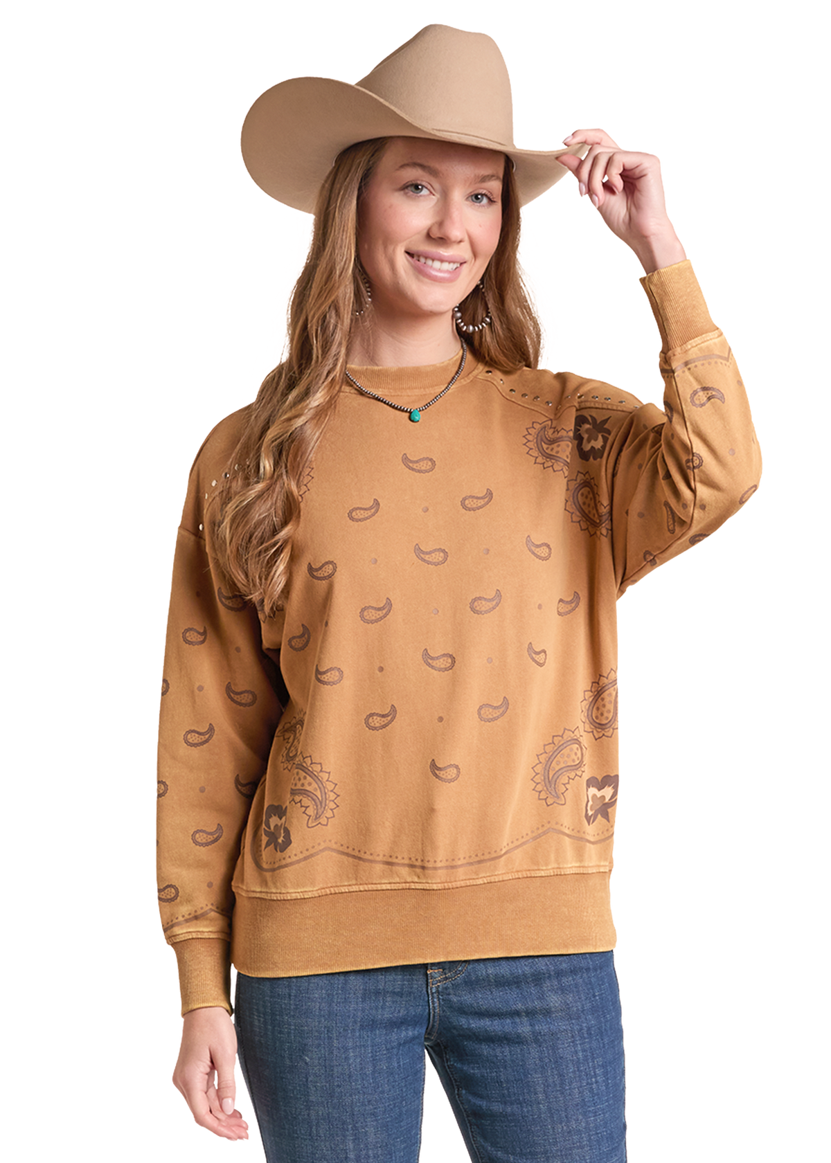 A woman wearing a tan cowboy hat and a tan long-sleeve crewneck sweatshirt with a brown paisley print, paired with blue jeans.
