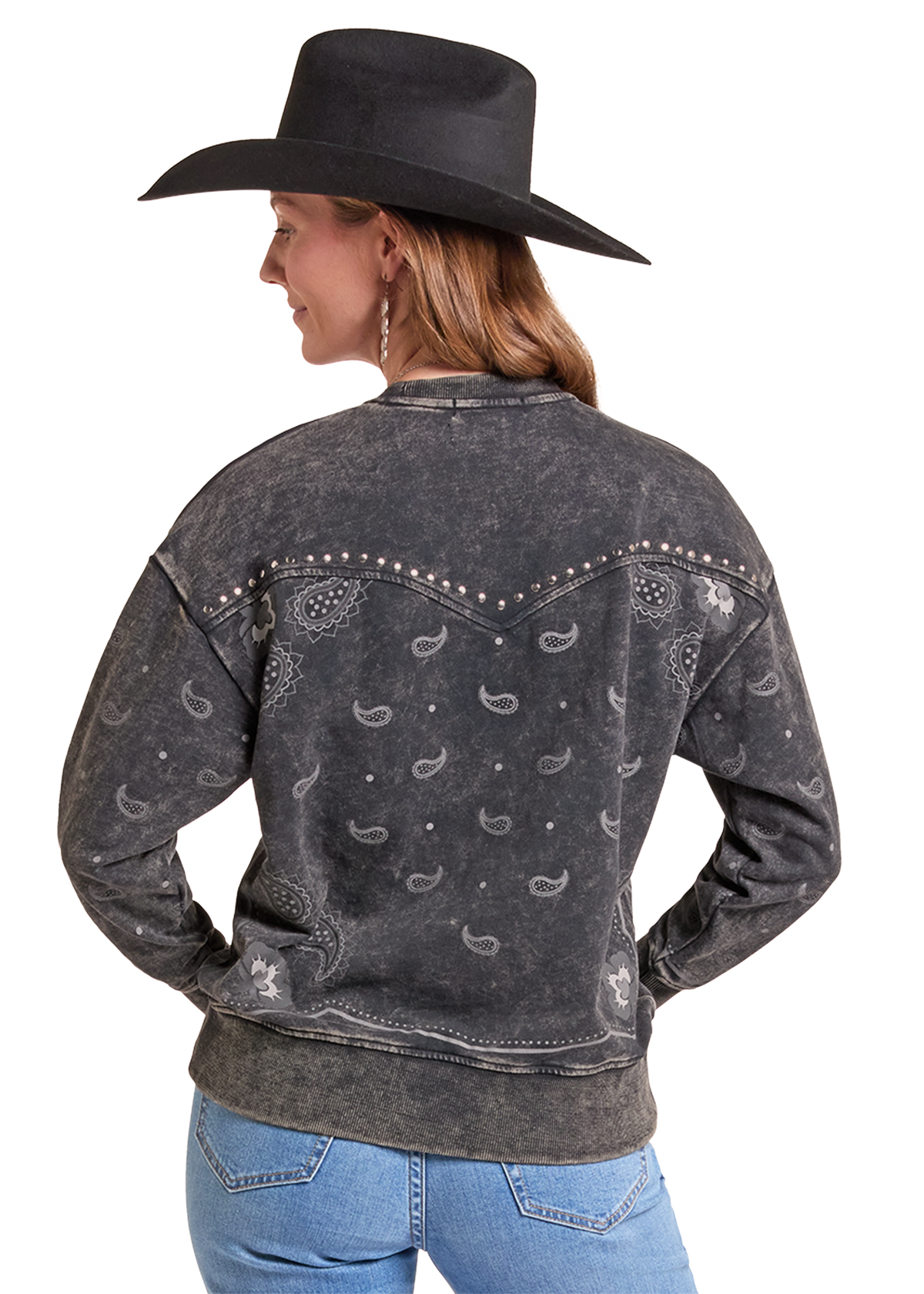 A woman shown from the back wearing a dark gray acid-wash western sweatshirt with a bandana print and silver studs, paired with a black cowboy hat and blue jeans, against a solid white background.