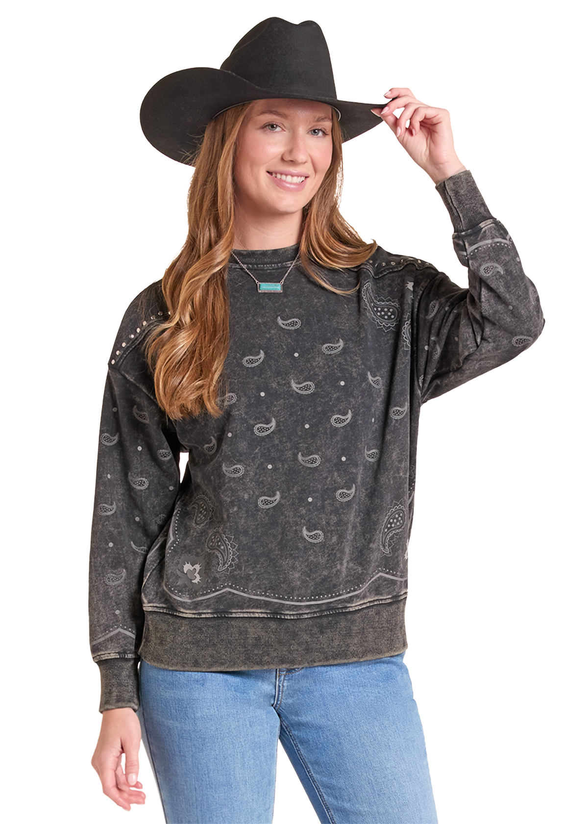 A woman wearing a dark gray acid-wash crewneck sweatshirt with a western bandana print, styled with a black cowboy hat and blue jeans against a white studio background.