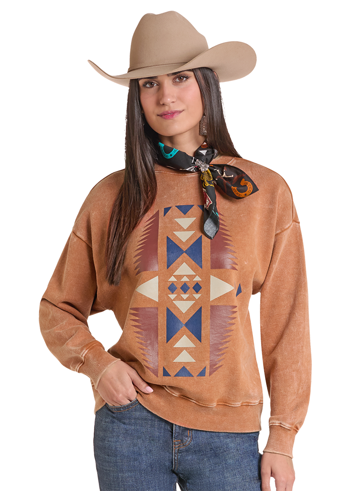 A woman modeling a tan western-style sweatshirt with a large geometric Southwestern-style print in blue, beige, and brown on the front. She is wearing a tan cowboy hat, a patterned neck scarf, and blue jeans against a plain white background.