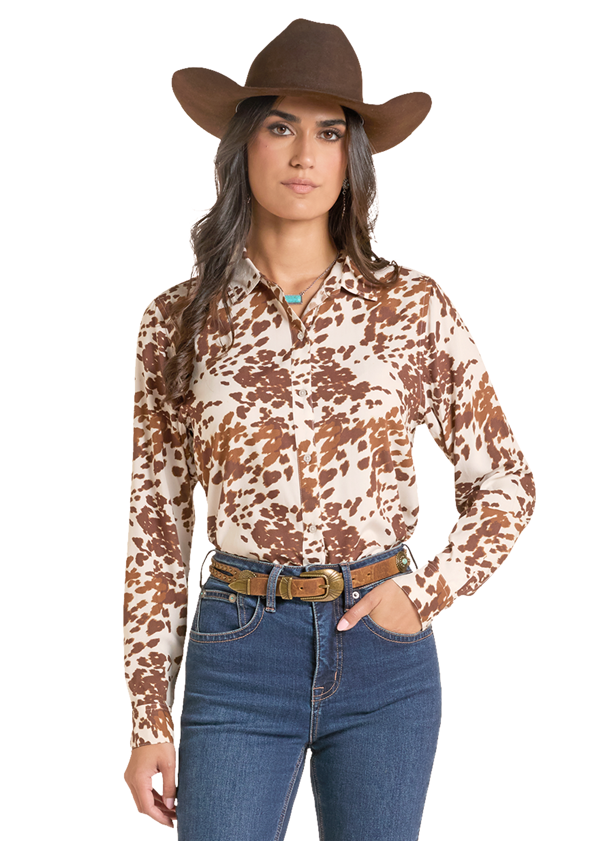 A woman modeling a long-sleeve button-up shirt with a brown and beige cow-print pattern, paired with a brown cowboy hat, blue jeans, and a brown belt against a plain white background.